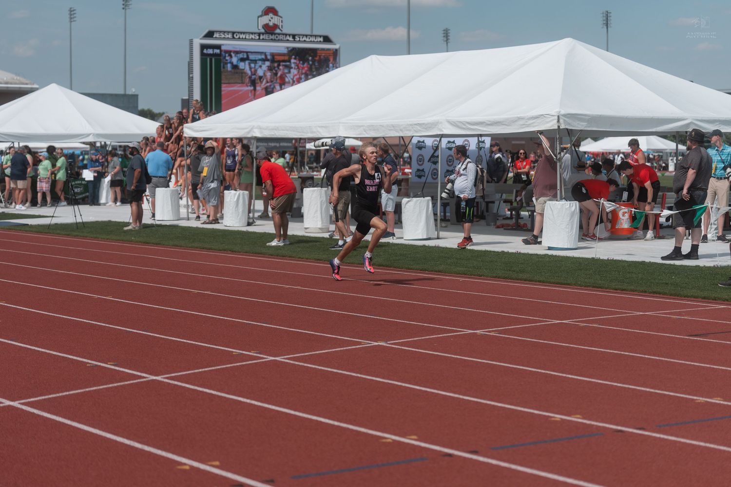 A male athlete sprints toward the finish line on a red track at a high school track and field meet.