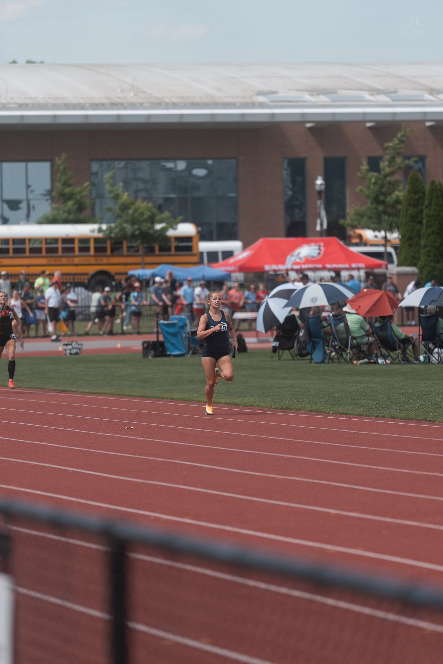 Female sprinter runs alone on a red track during a high school state championship track and field event.