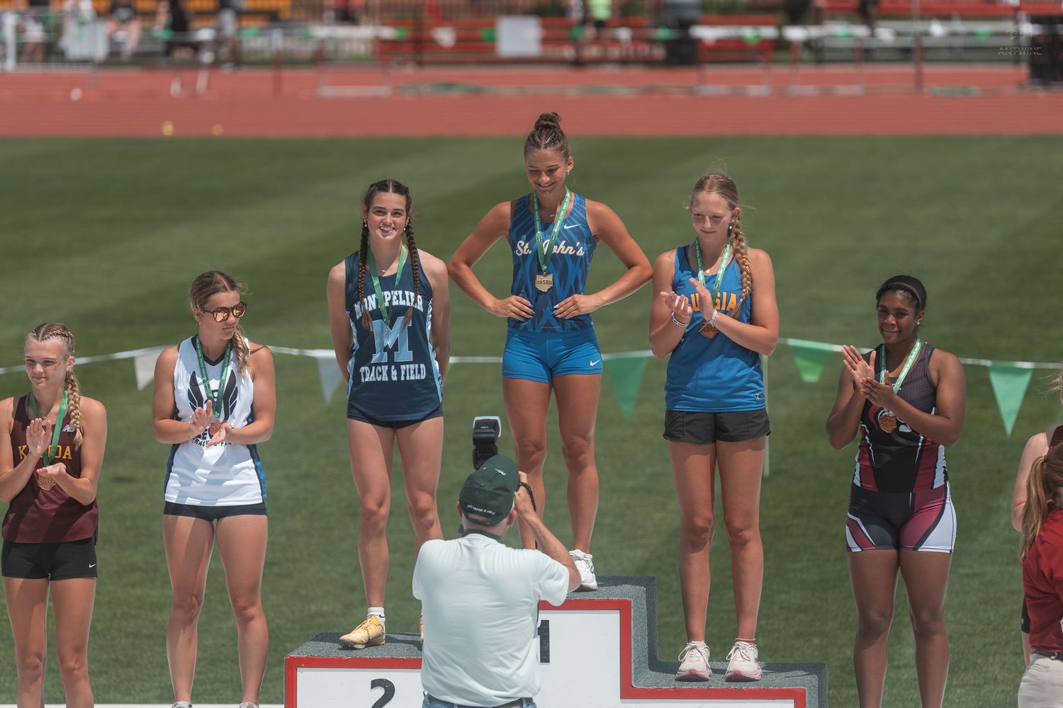 Female long jump competitors stand on numbered award podium at OHSAA state track championship.