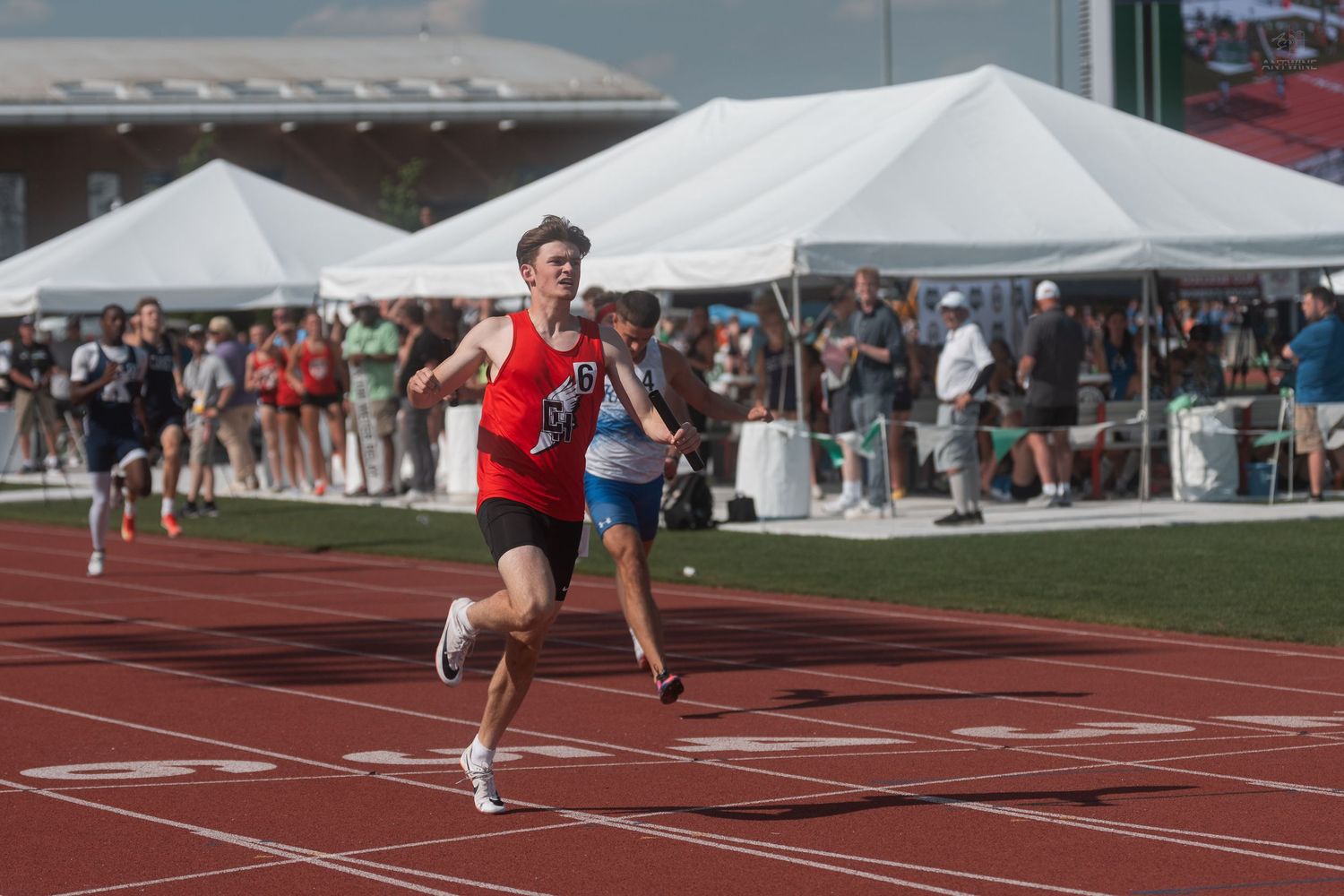 Athlete in red uniform wins a sprint race at an outdoor high school track and field championship meet.