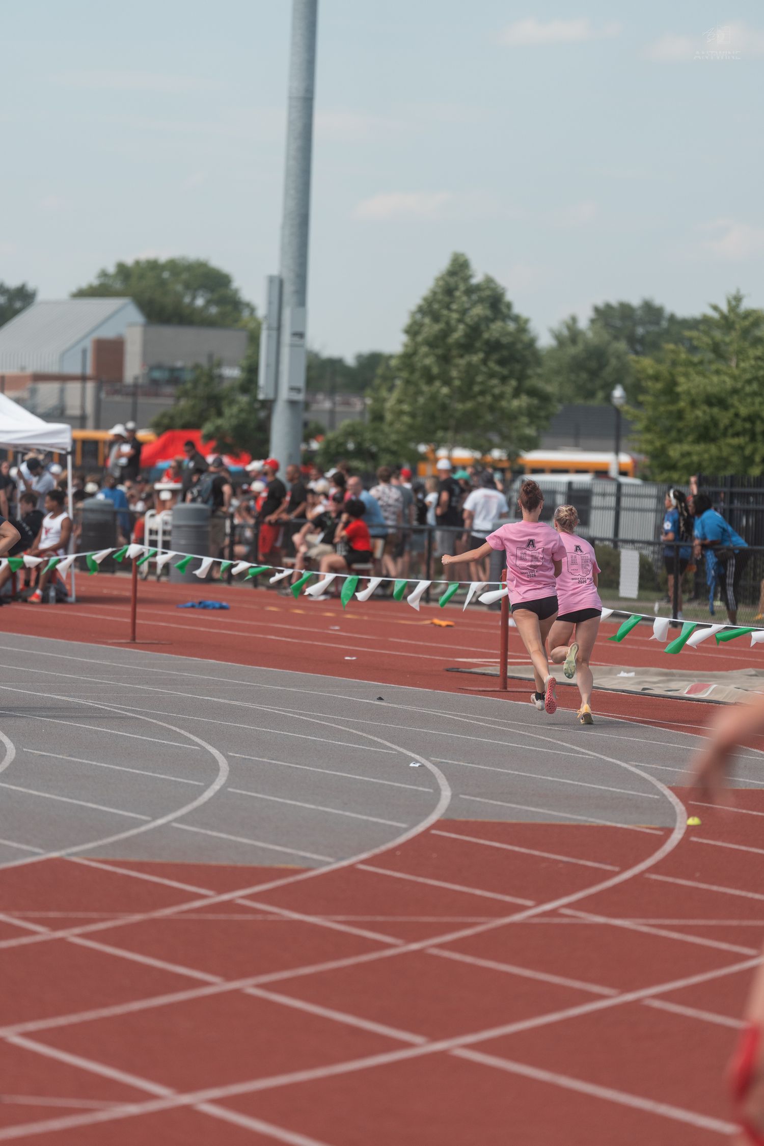 Two female athletes in pink shirts pass baton during relay race on red track.