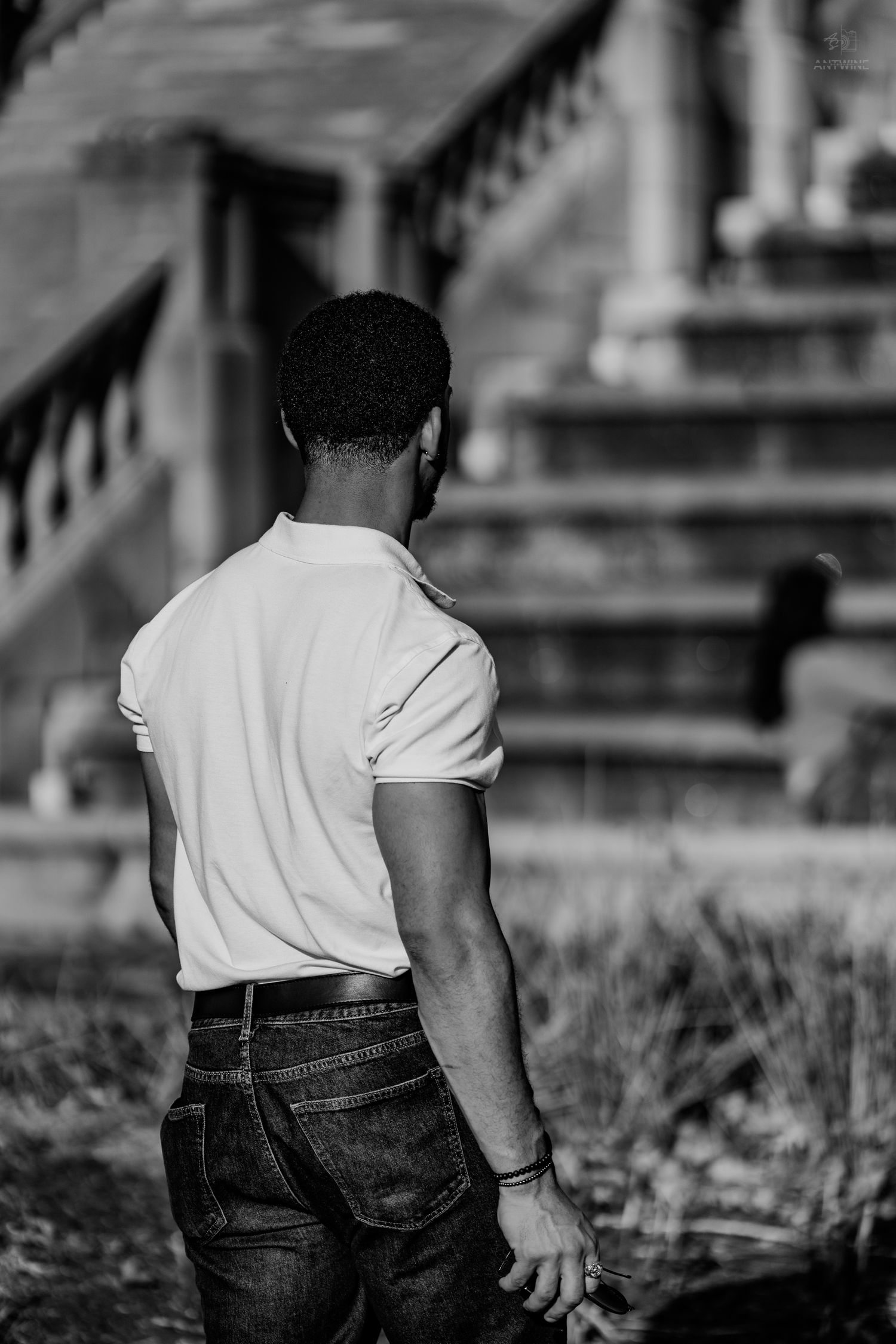 Black and white rear view of a man in a white t-shirt standing near stone steps.