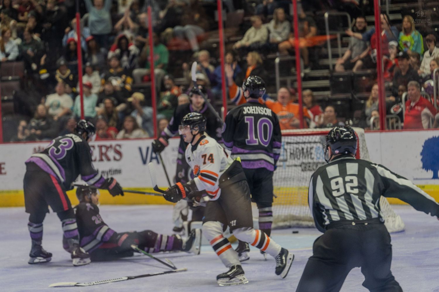 Hockey players from opposing teams battle for the puck near the boards during a physical minor league game.