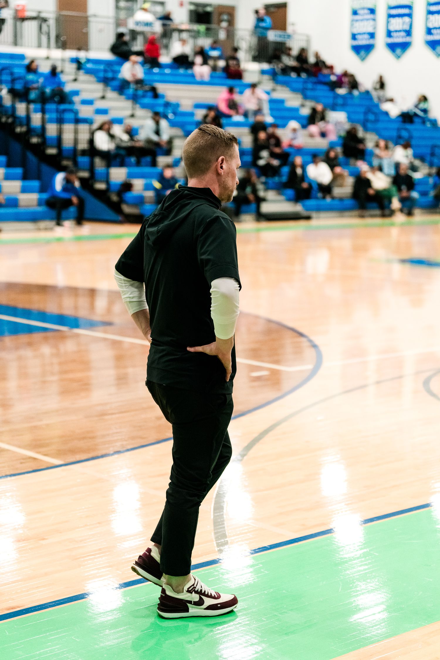 A coach in black stands on the sideline watching a girls high school basketball game at Warriors home court.