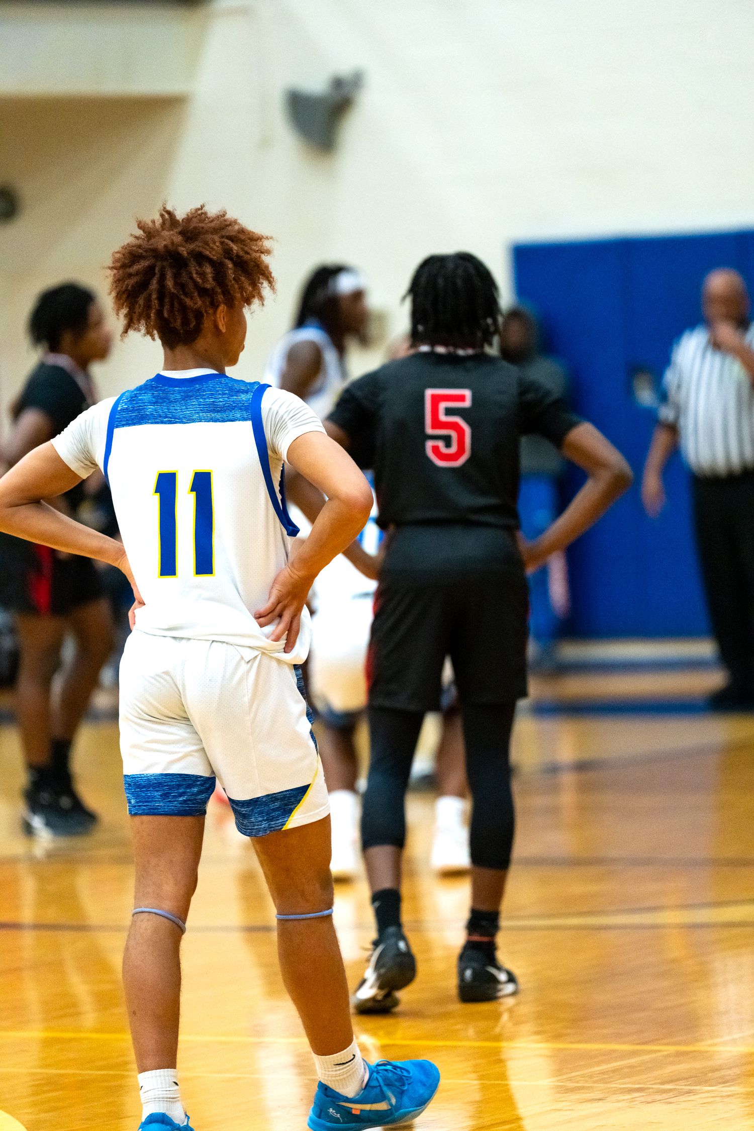 Player #11 in blue uniform faces opponent #5 in black during high school basketball game.