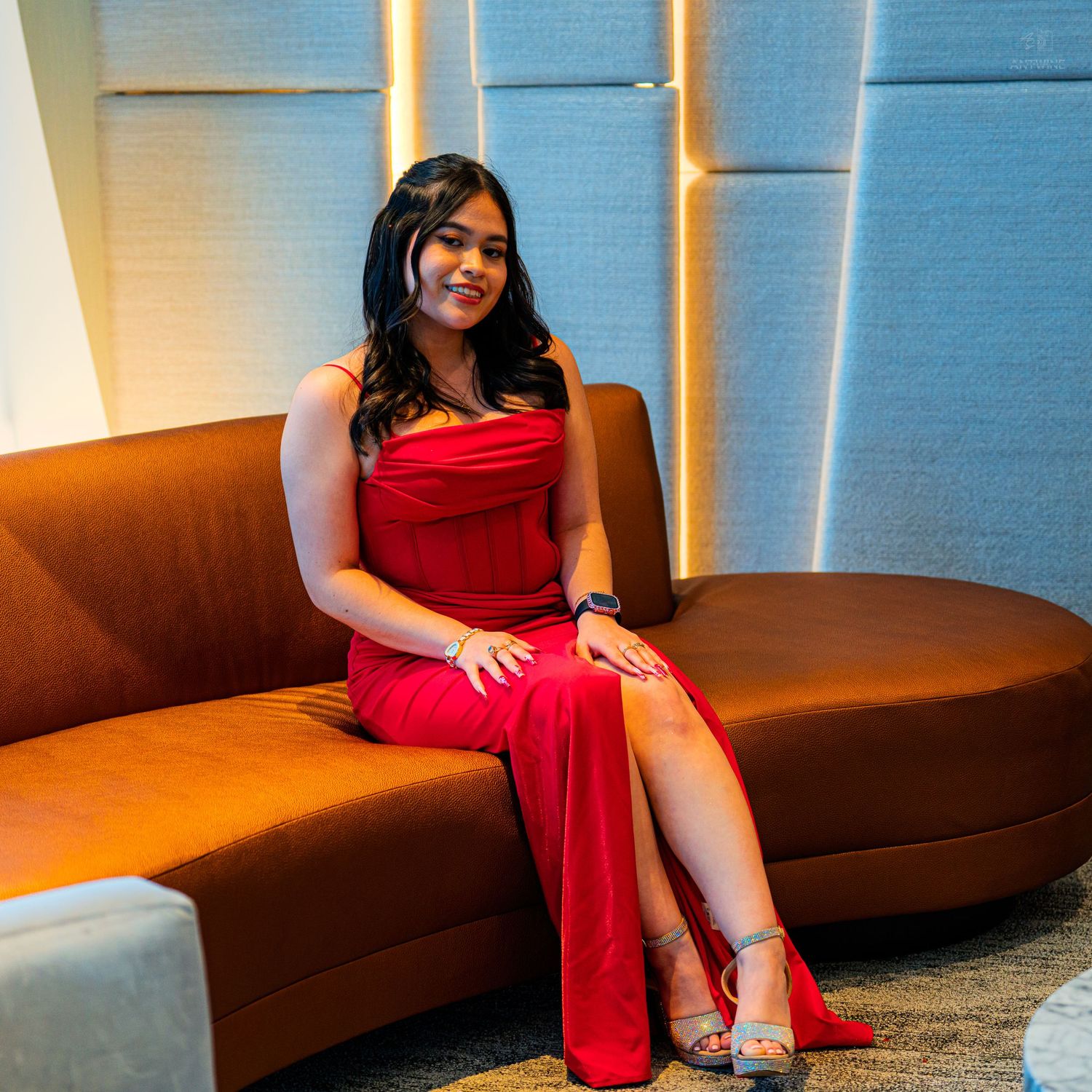 Young woman in red dress seated on brown curved sofa in modern interior.