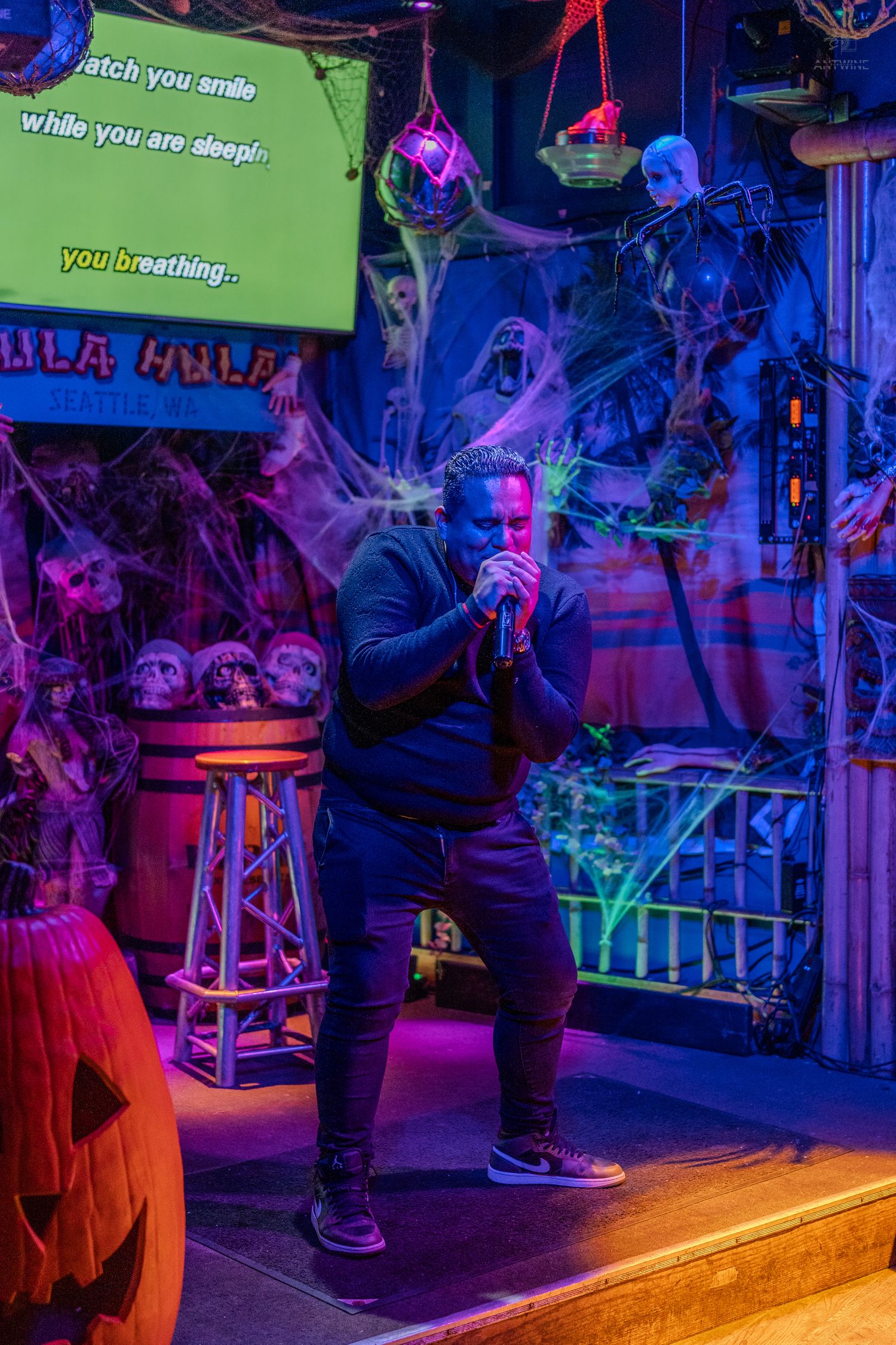 Man performing karaoke on a spooky Halloween-decorated stage with blue and purple lighting.