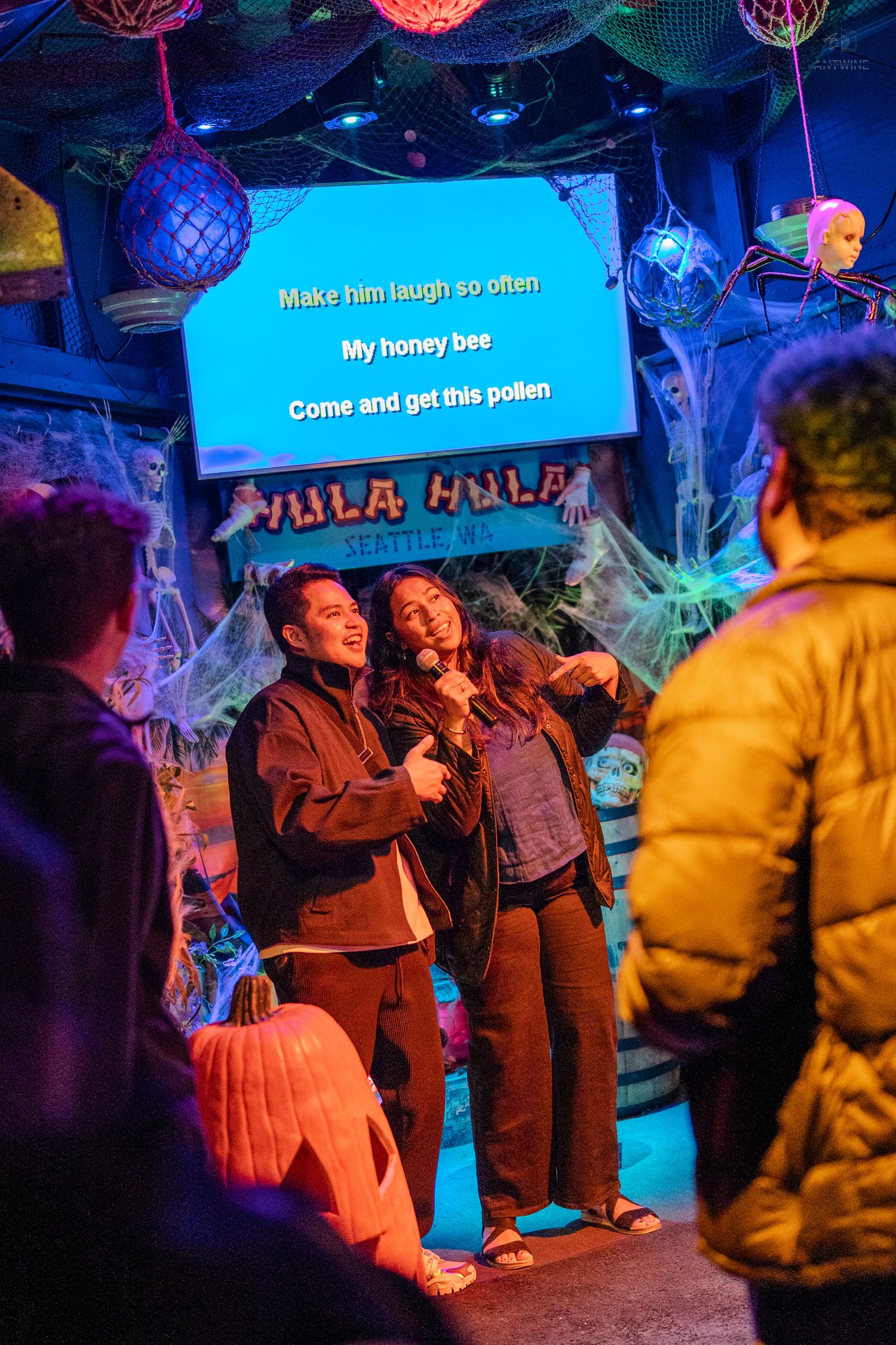 Two people singing karaoke together at a Halloween-themed venue with festive decorations.