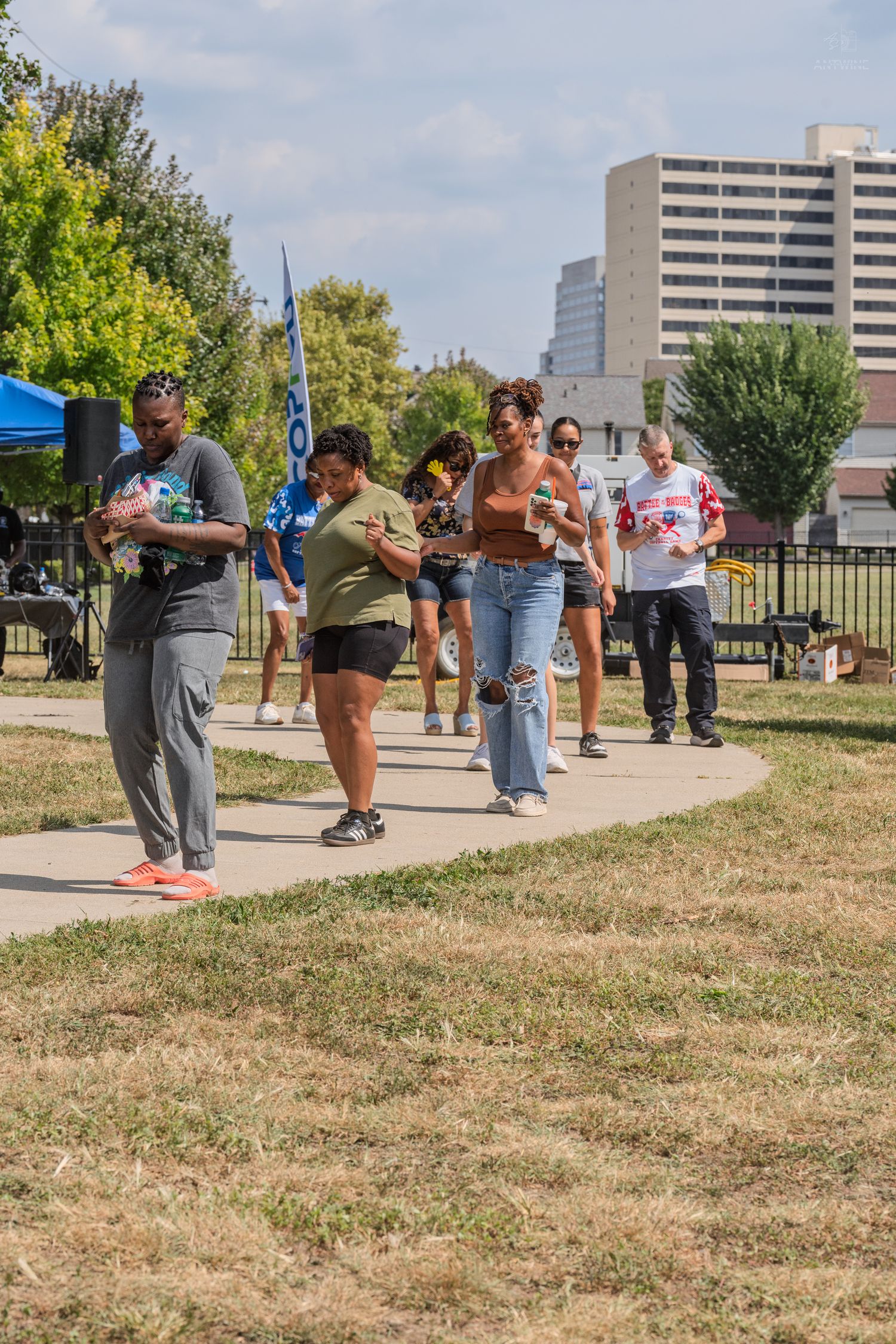 Group of people walking along a sunny park path carrying food at a community event.