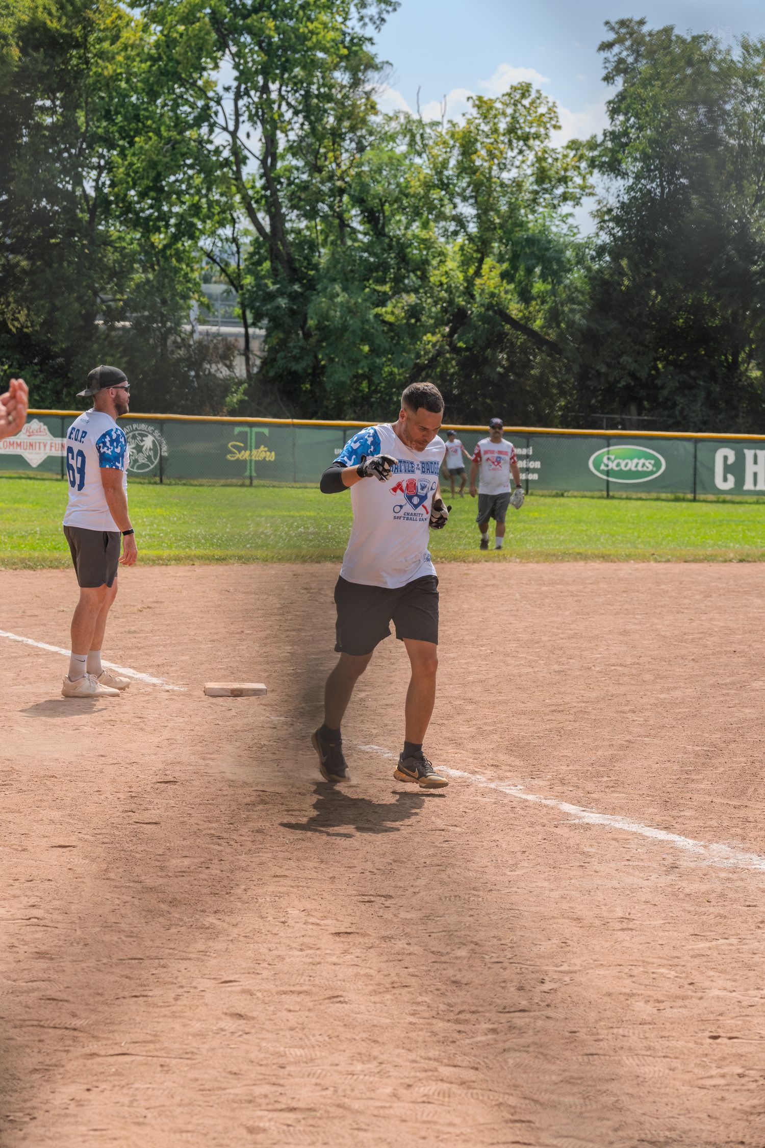Player celebrates reaching base during a sunny outdoor softball game on a dirt field.