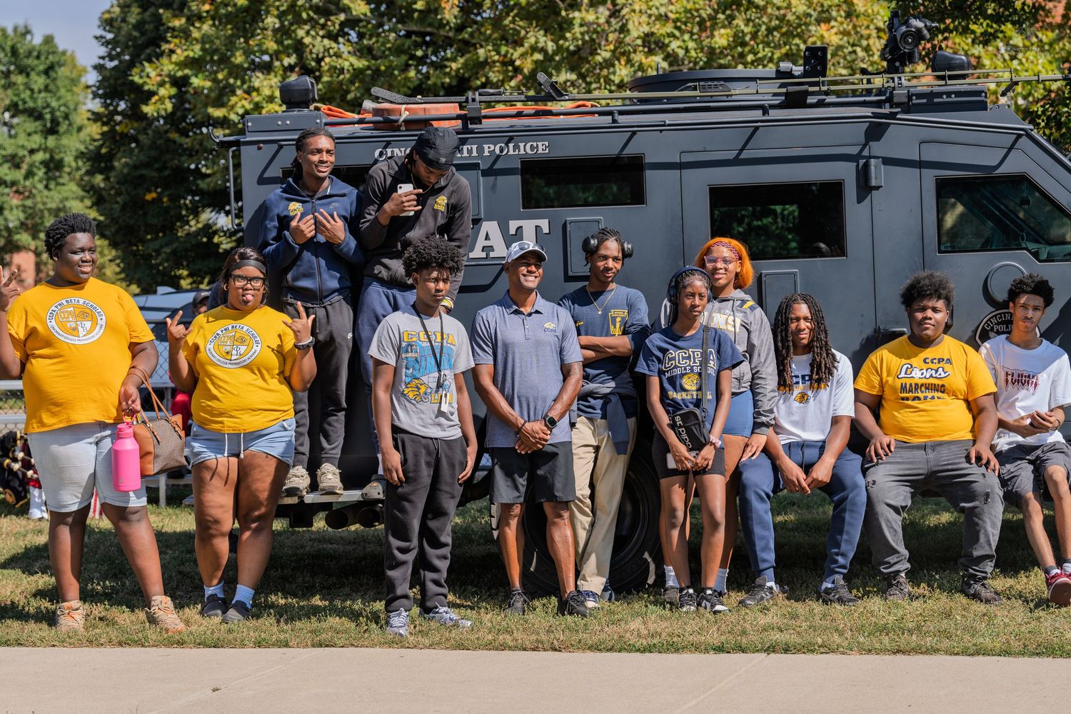 Group of people posing outdoors near an ATF vehicle on a sunny day, wearing casual and yellow shirts.