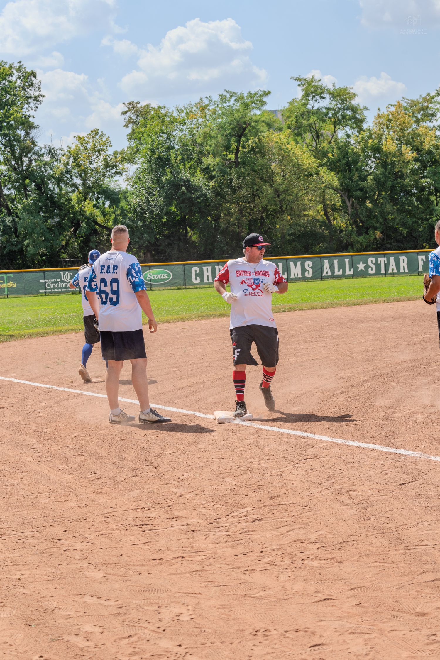 Players competing in a charity softball game on a sunny summer day at Chris Helms All-Star Field.