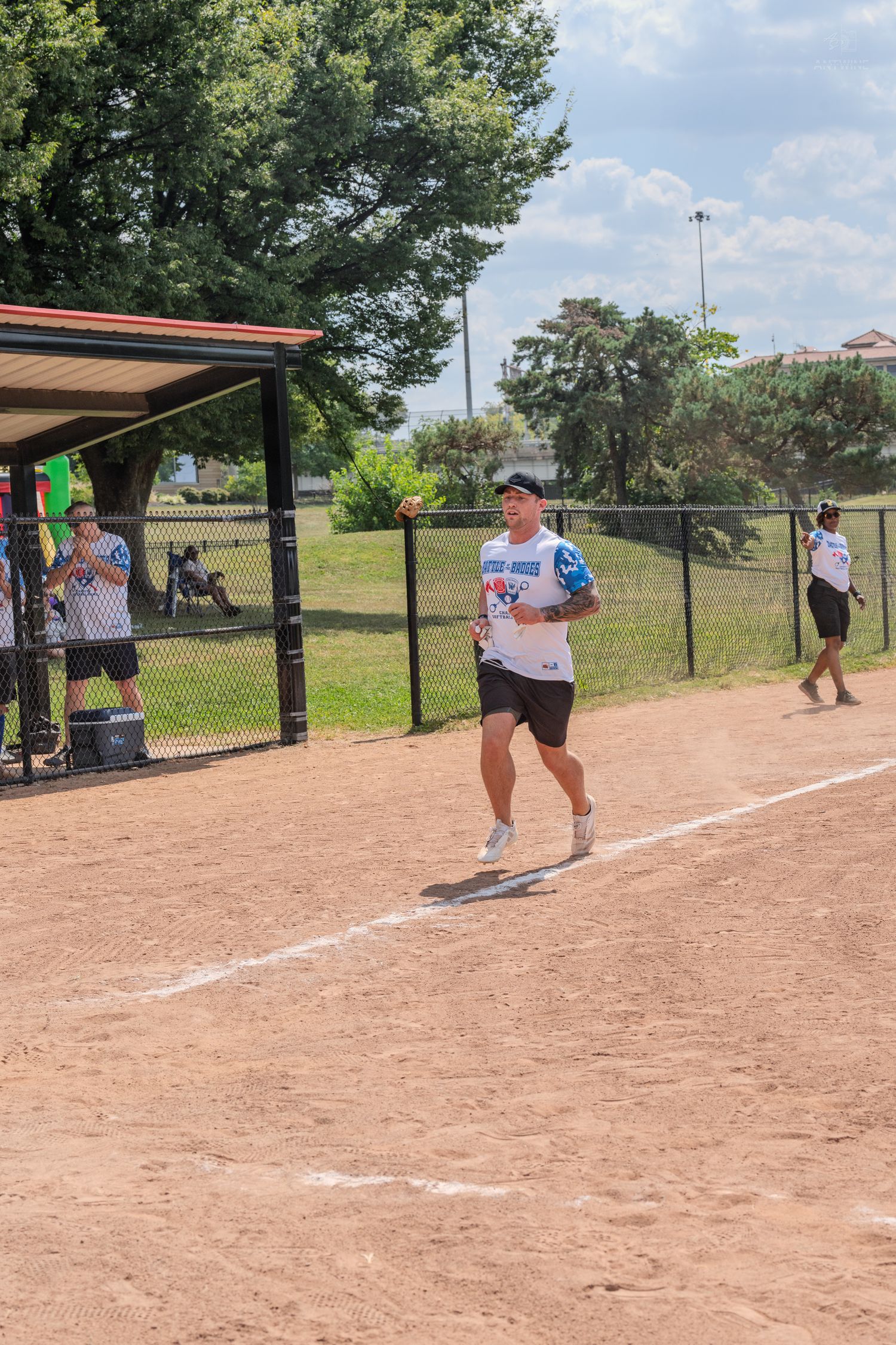 Male softball player in white uniform running the base path on a sunny summer day.
