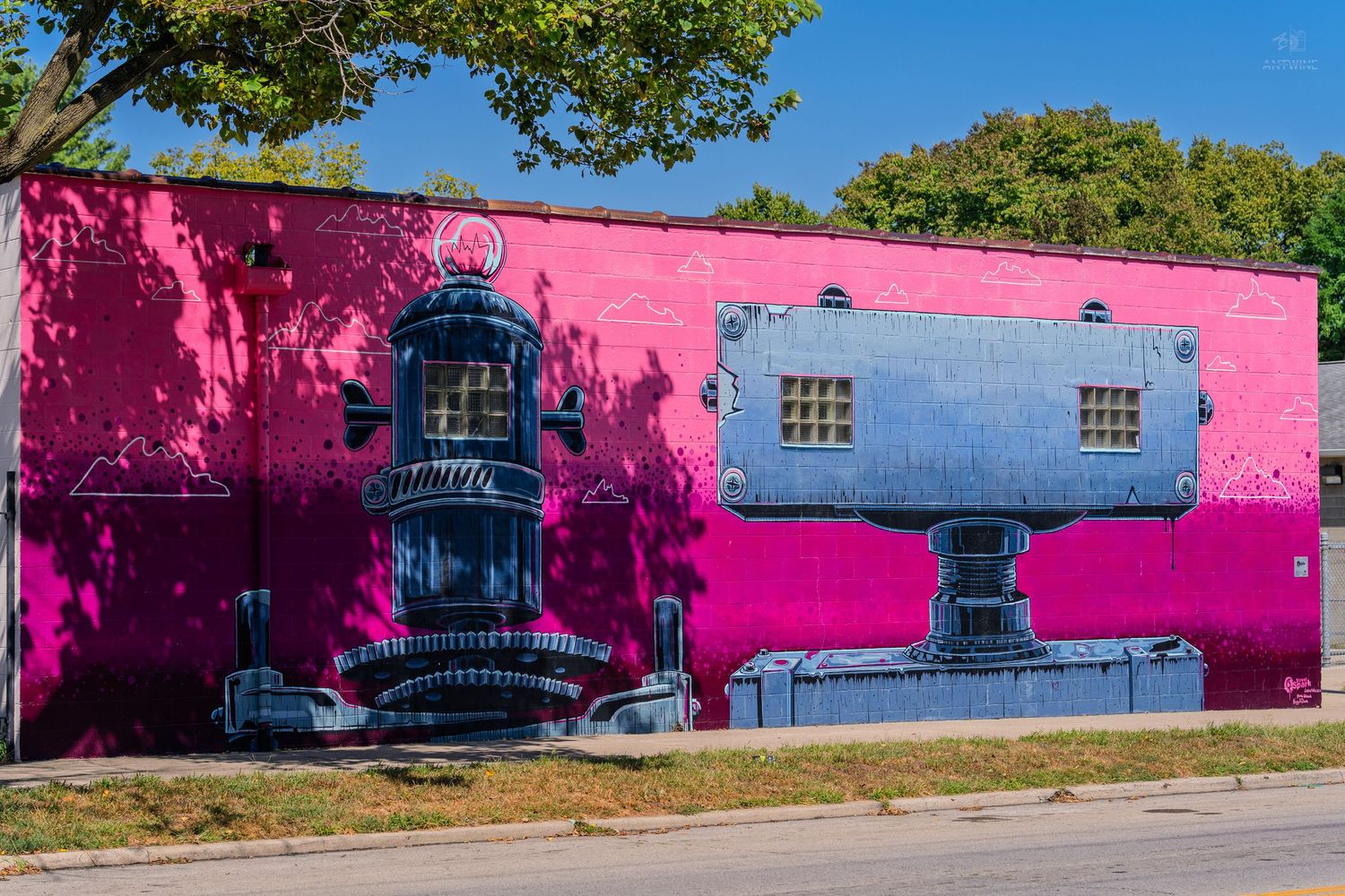Vibrant pink building wall featuring large industrial robot mural street art under clear blue sky.