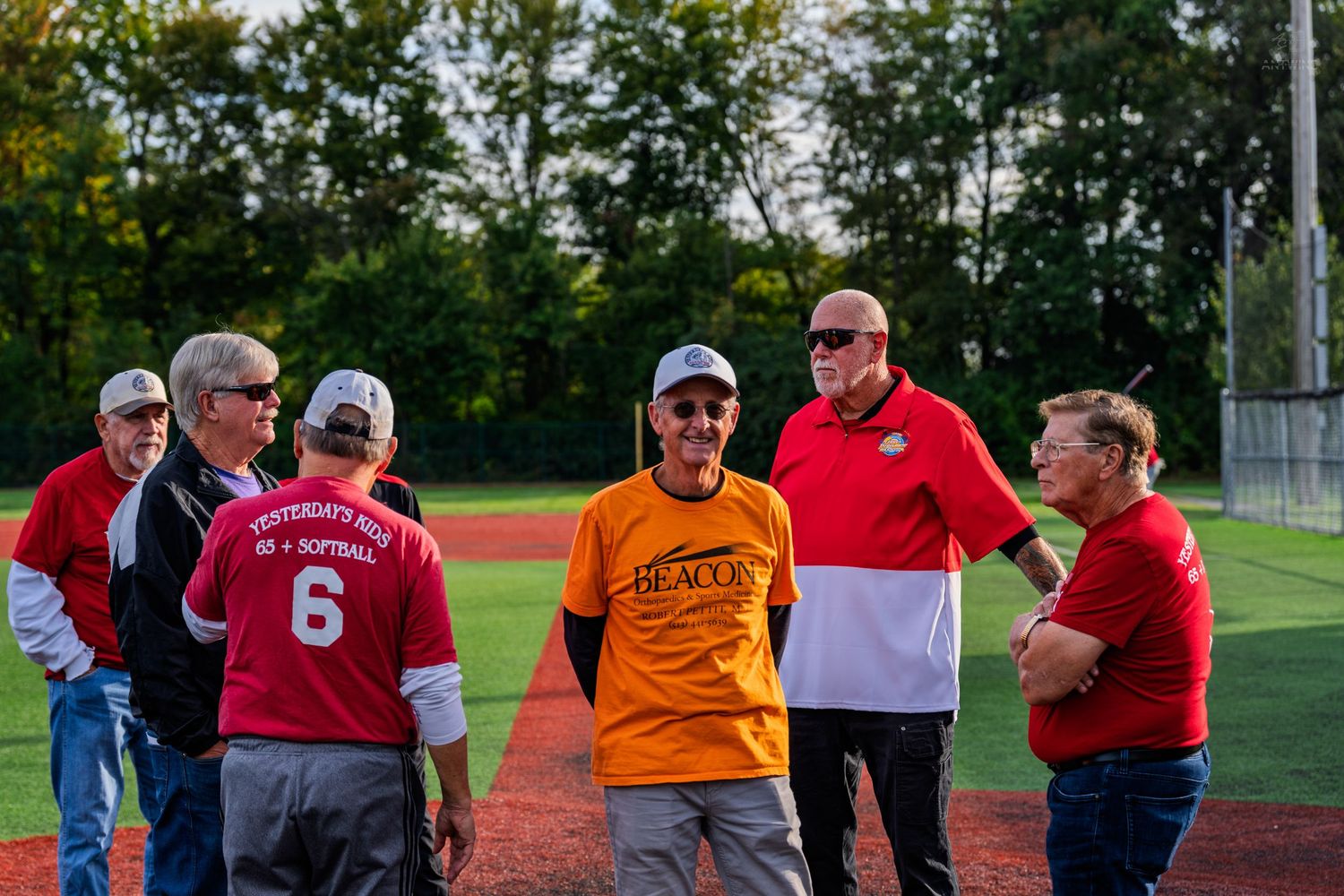 Group of adults socializing on a baseball field during an evening recreational softball game.