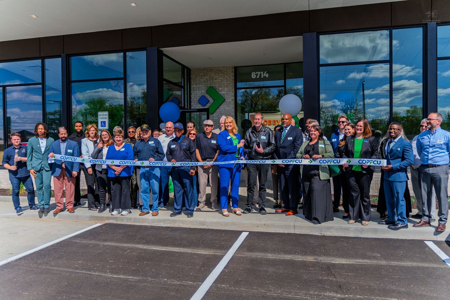 Group of professionals celebrating a ribbon cutting ceremony outside a modern commercial building on a sunny day.