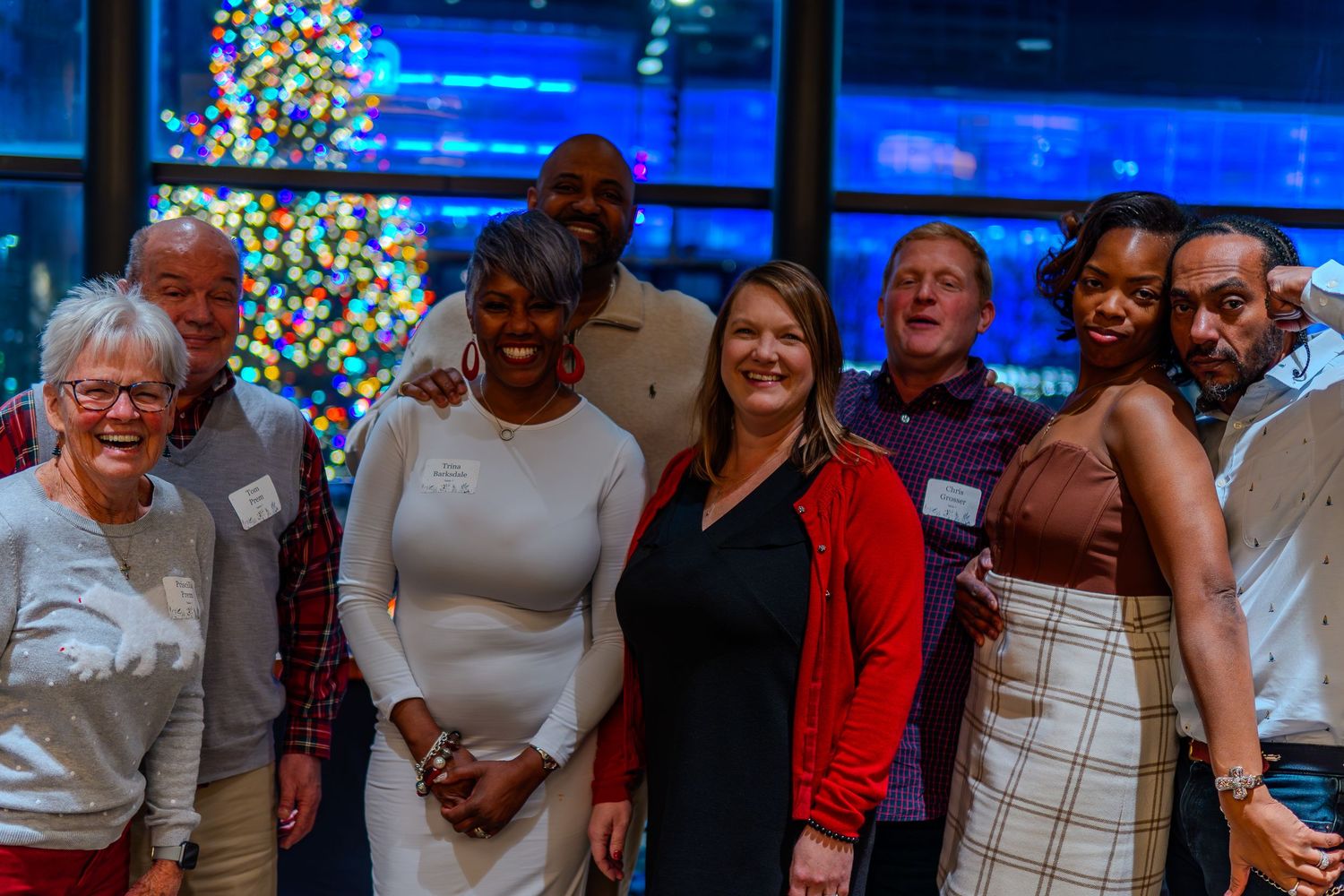Group of diverse professionals smiling together at a festive holiday party with a decorated Christmas tree in the background.