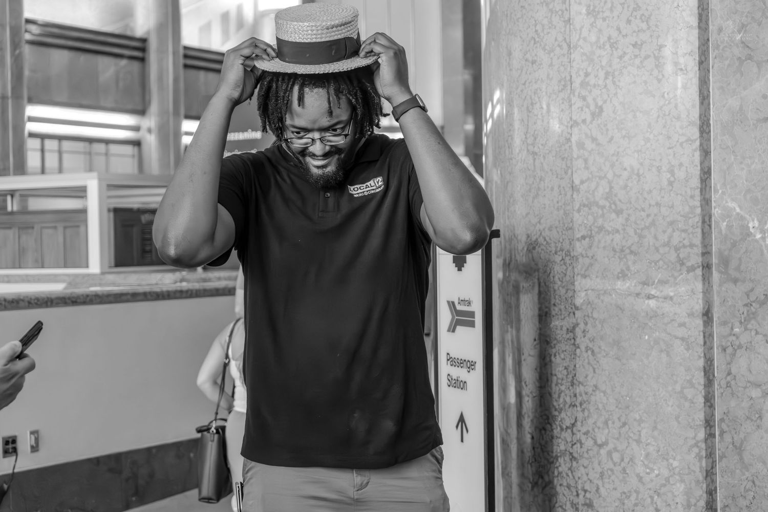 A happy man tries on a straw fedora hat outdoors in a black and white photo.