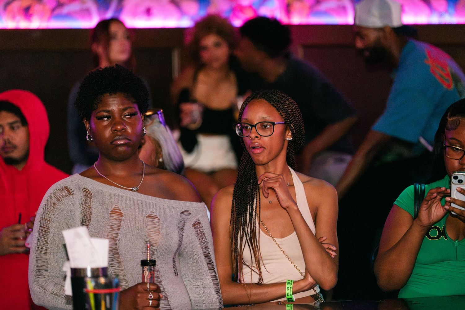 Two women standing together at a nightclub event, holding drinks under warm ambient lighting.