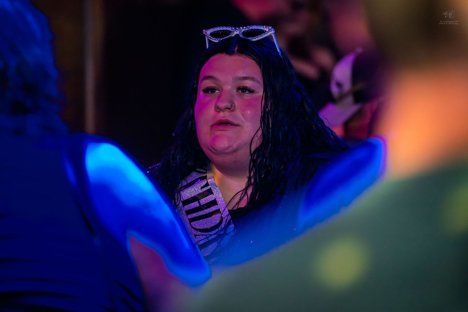 Woman with sunglasses on her head illuminated by blue light at a night event.