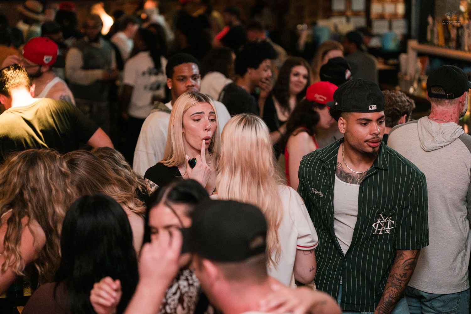 Diverse group of young adults socializing in a packed trendy bar or nightclub venue.