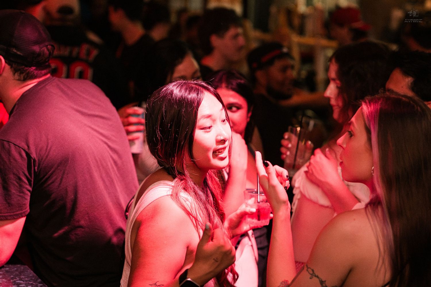 Young woman laughing and socializing with friends under red lights at a nightclub.