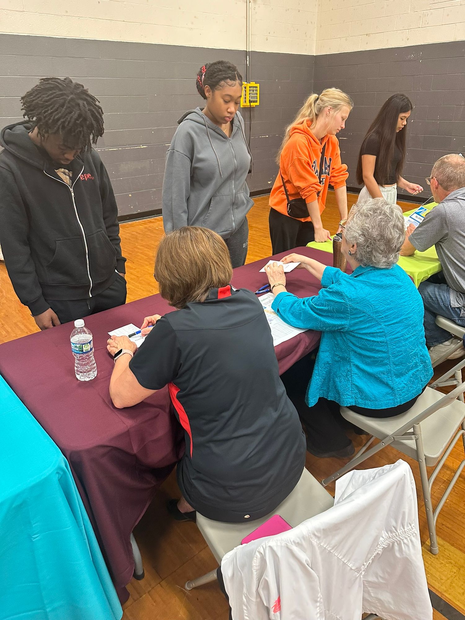 People registering at a table with purple tablecloth in a school gymnasium during a community event.