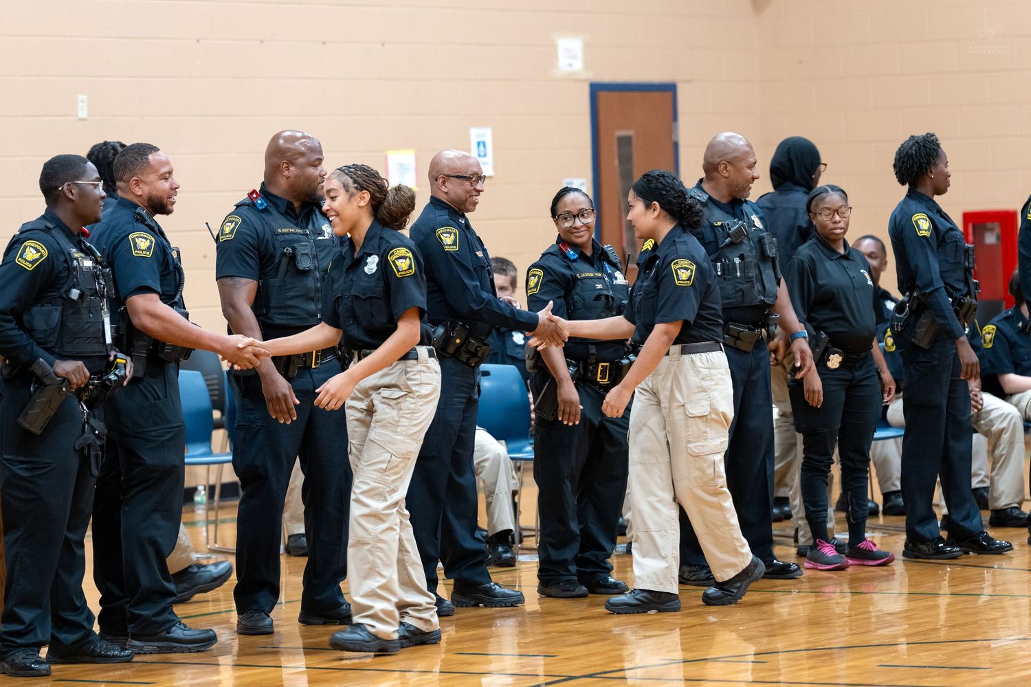 Law enforcement officers in uniform shaking hands during a formal ceremony inside a school gymnasium.