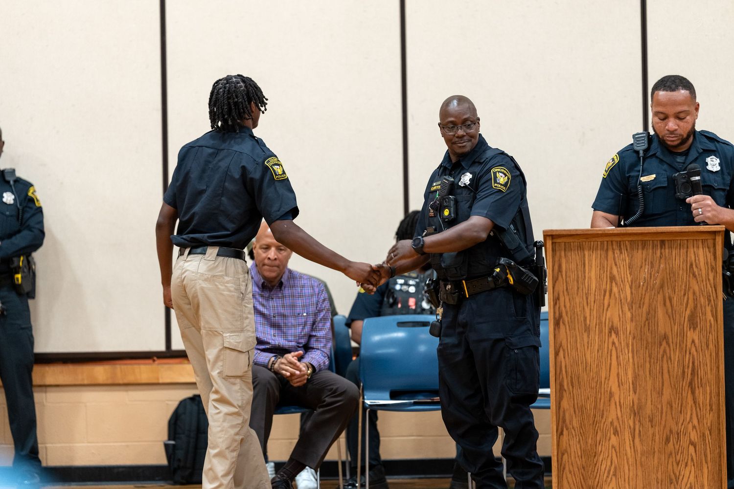 Police officers in uniform shake hands during an official ceremony in a conference room setting.