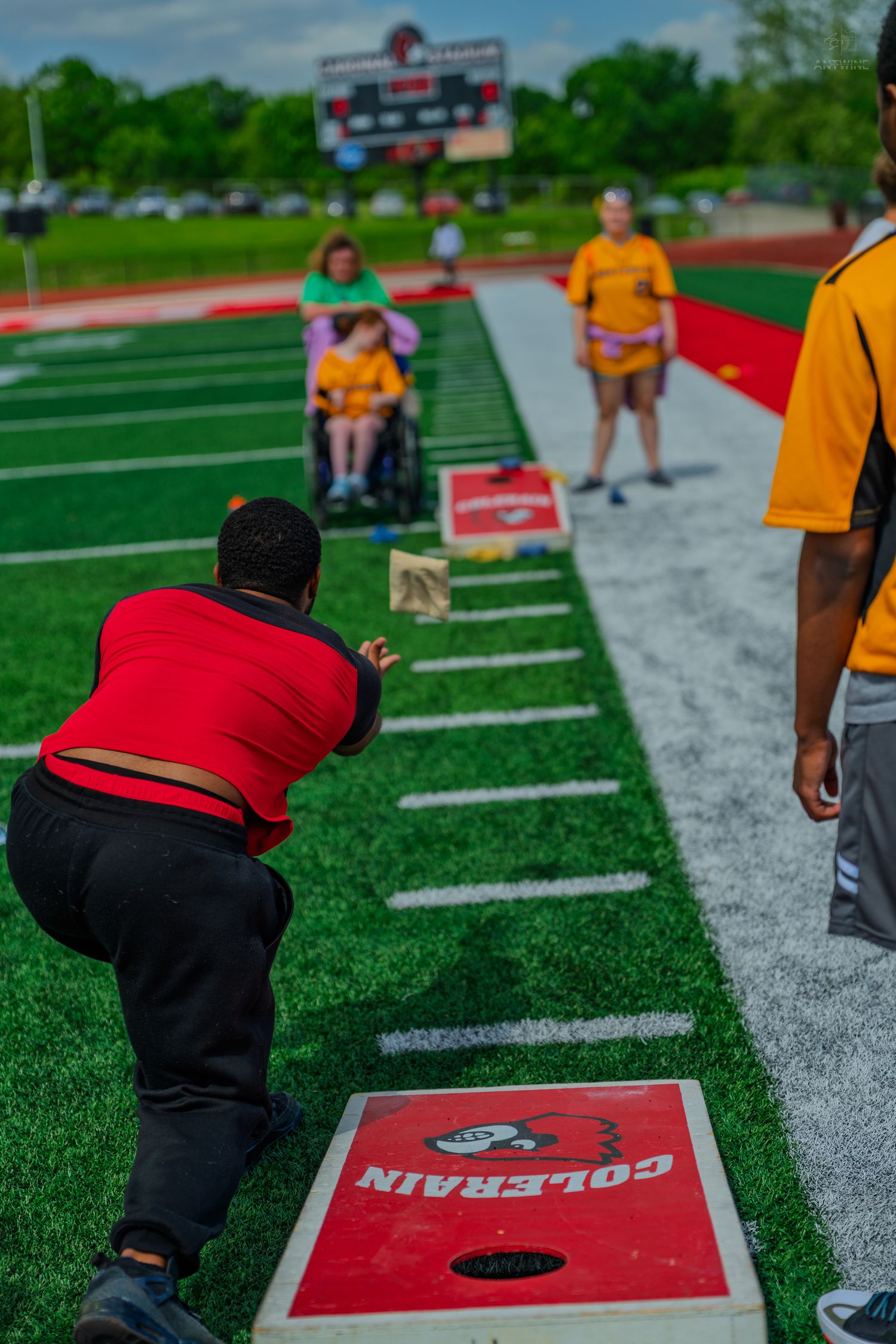 Players enjoy a game of cornhole on a Colerain football field, with a wheelchair user participating in the fun.
