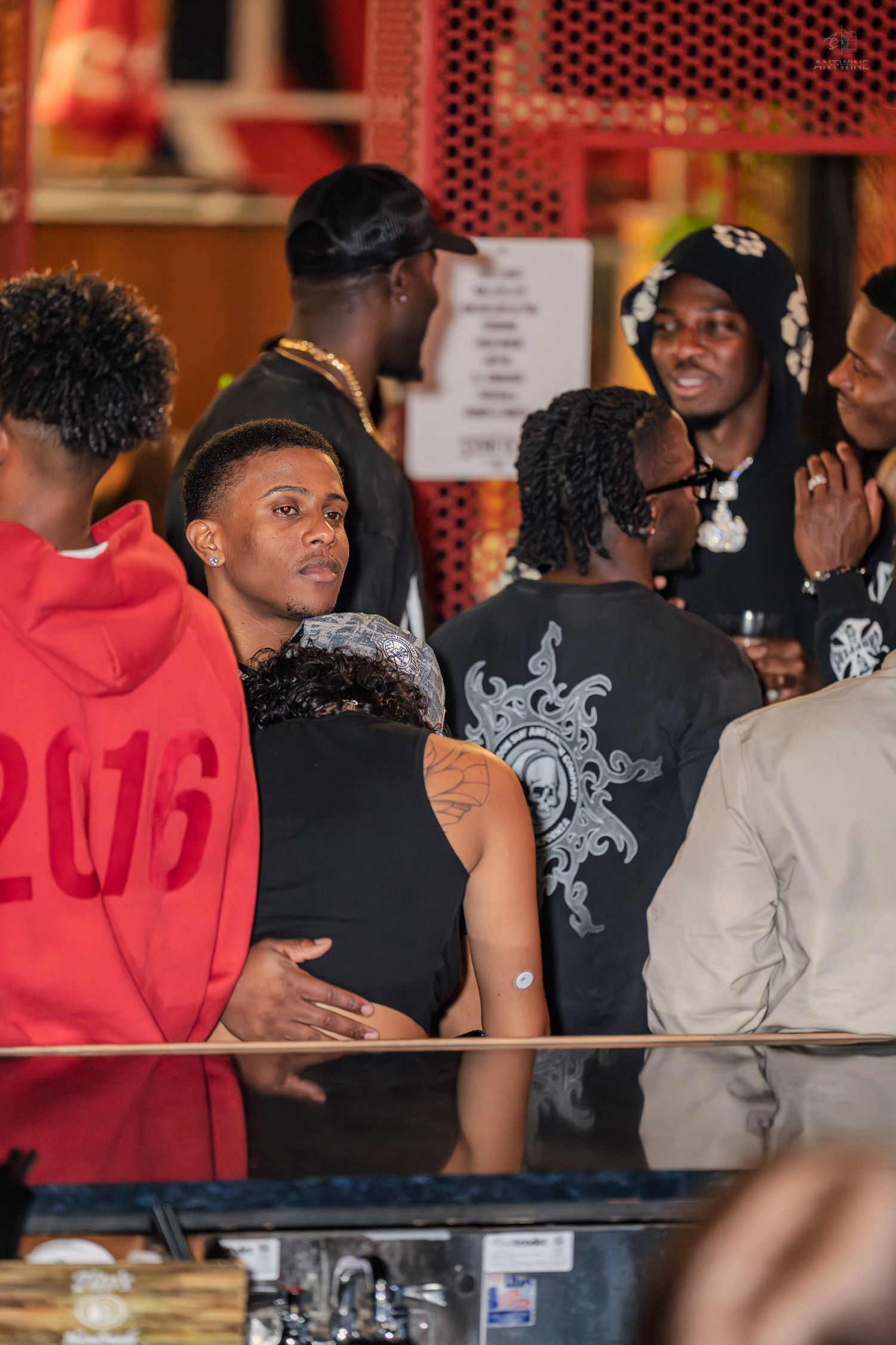 Group of people socializing in a crowded bar with colorful outfits and accessories.