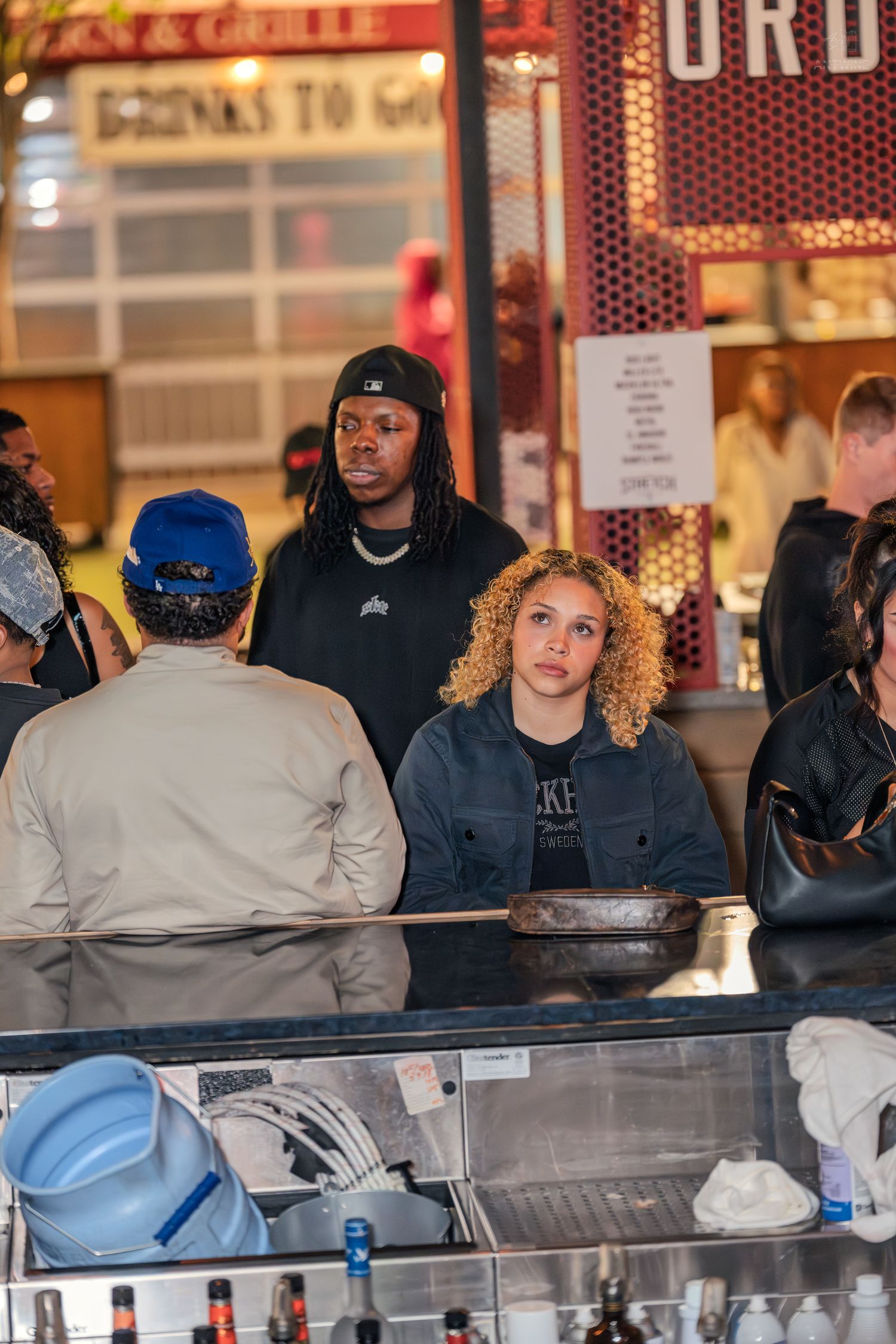 Young adults gathered at a nightclub bar counter under bright signage in a lively venue.