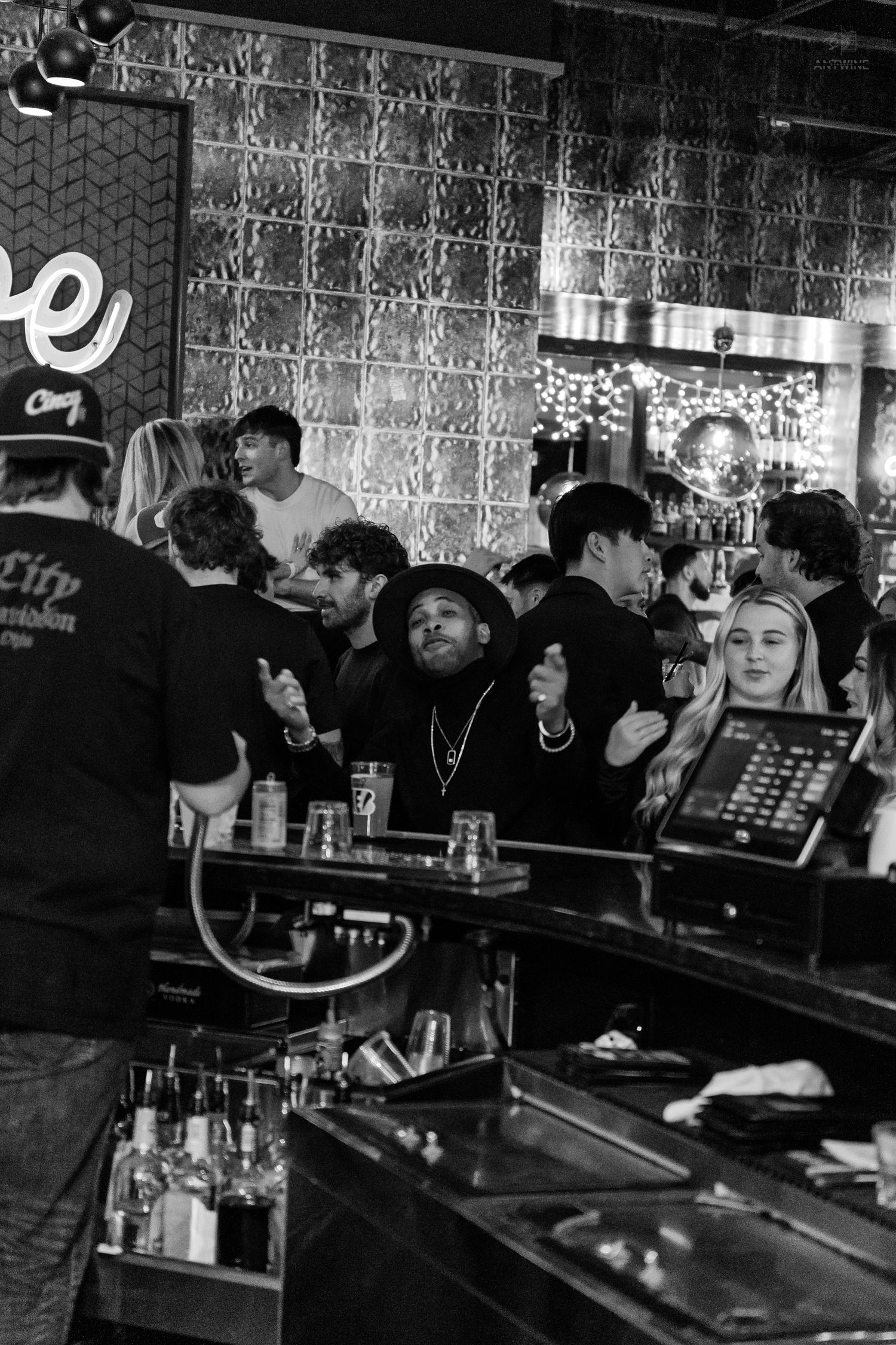 Black and white photo of a lively crowd gathered around a nightclub bar counter.