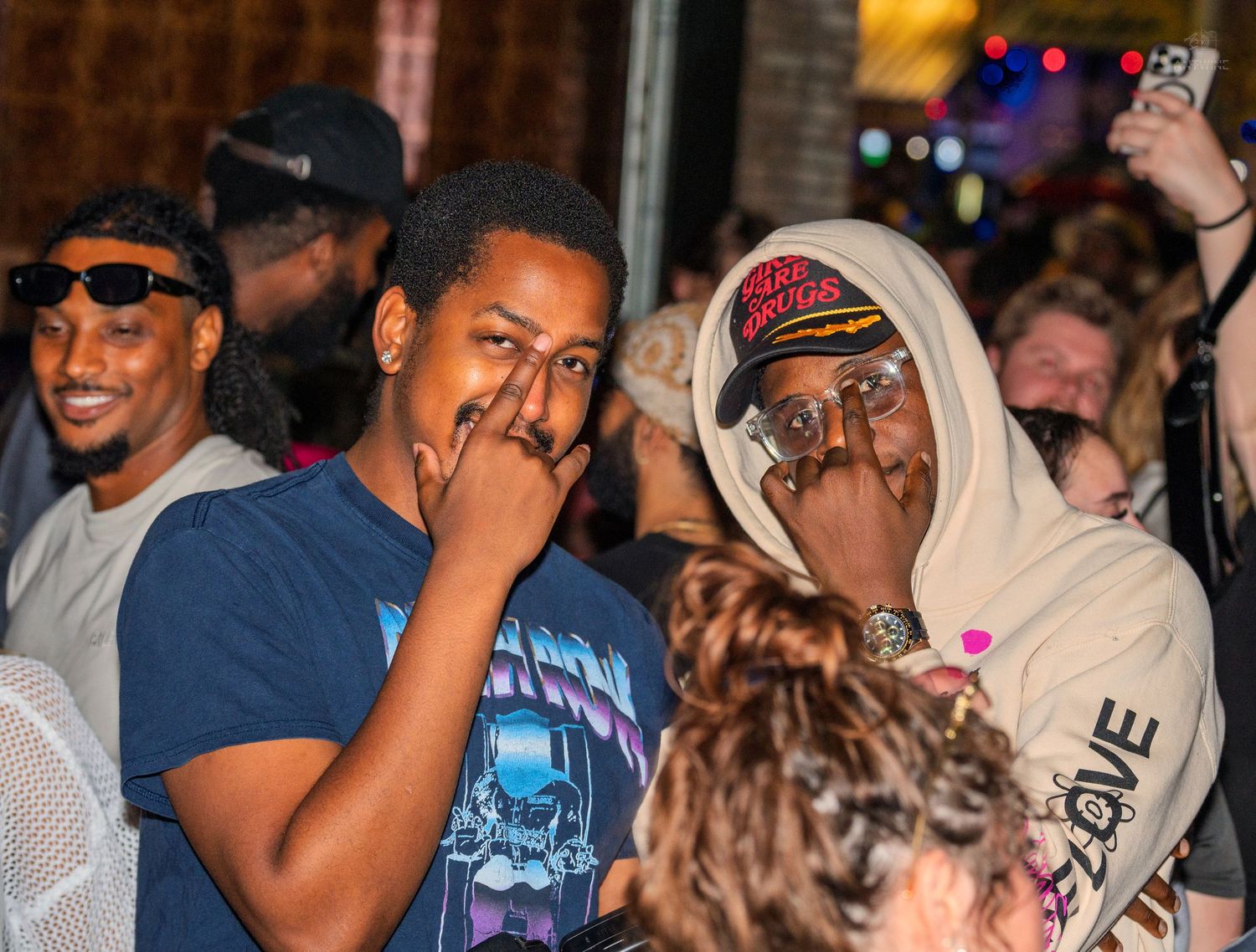Two young men covering their mouths with hands while standing in an outdoor crowd at night.