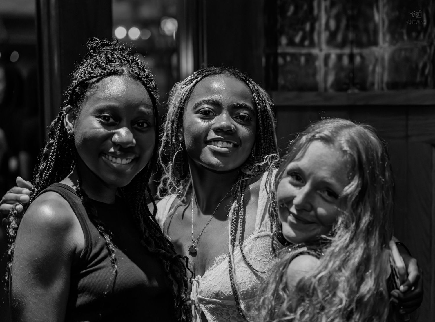 Three smiling young women posing together in a black and white nightlife photo.