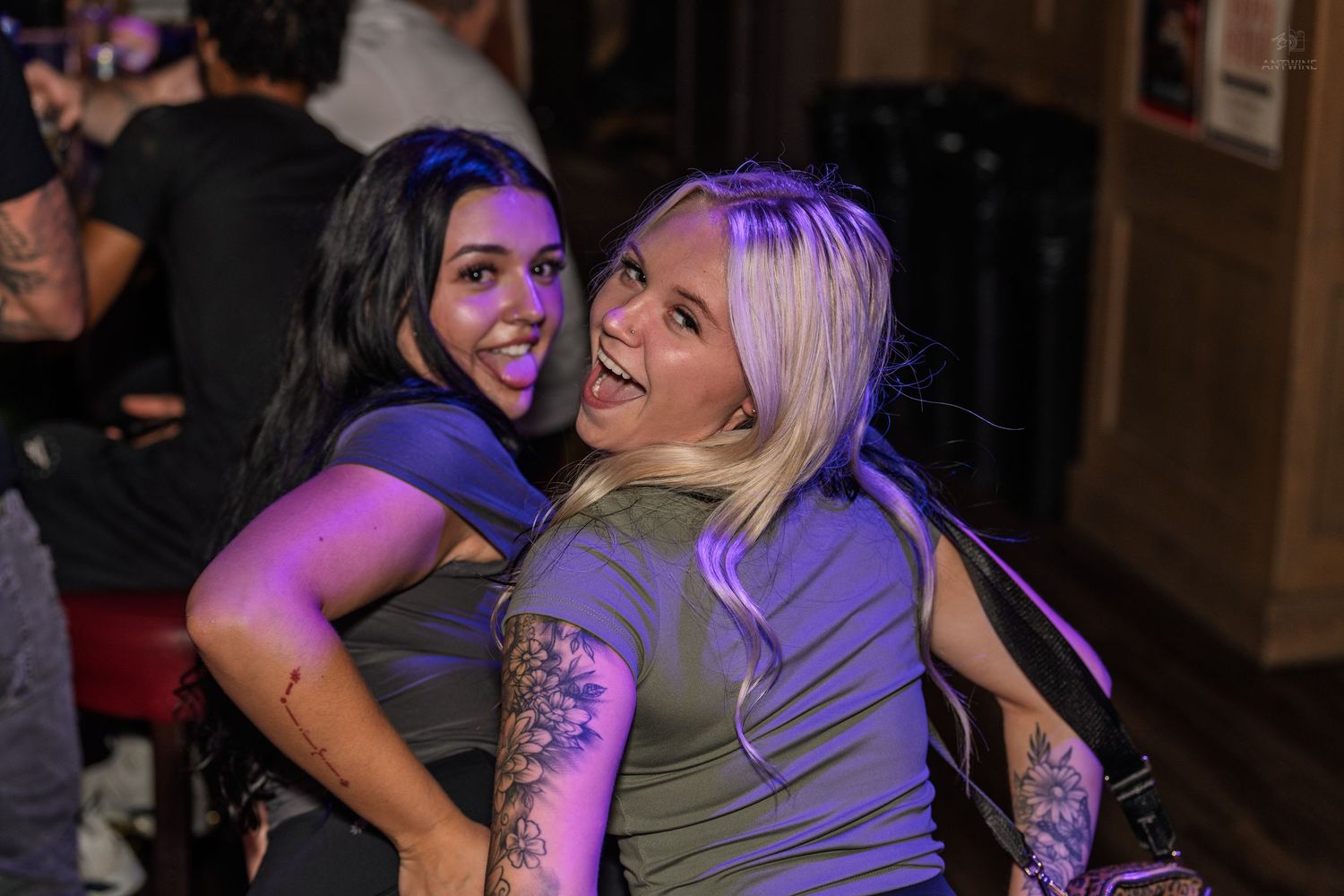 Two women hugging and laughing together under purple lights at a nightclub.