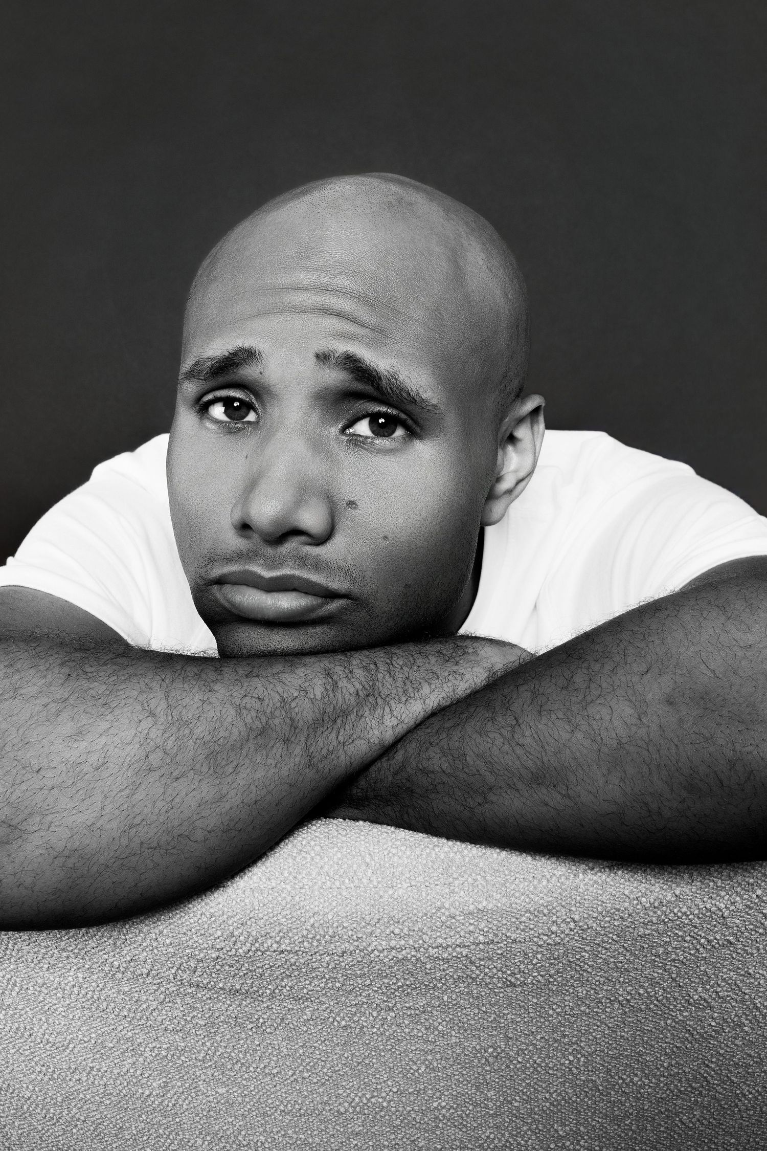Sad bald Black man in white t-shirt resting chin on crossed arms, emotional black and white portrait photo.