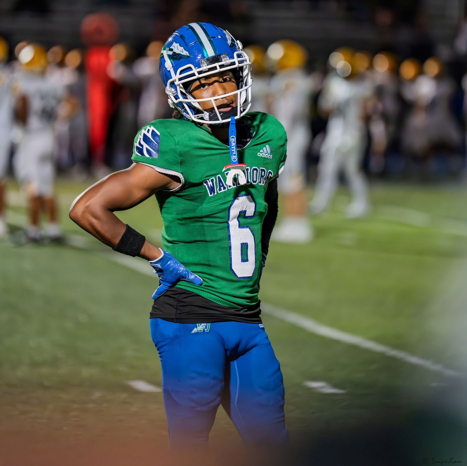 A football player wearing green jersey number 6 stands on the sideline during a night game.