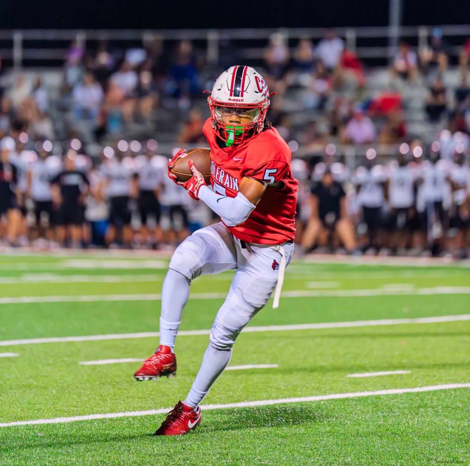 Colerain football player in red uniform catches the ball during a night game.