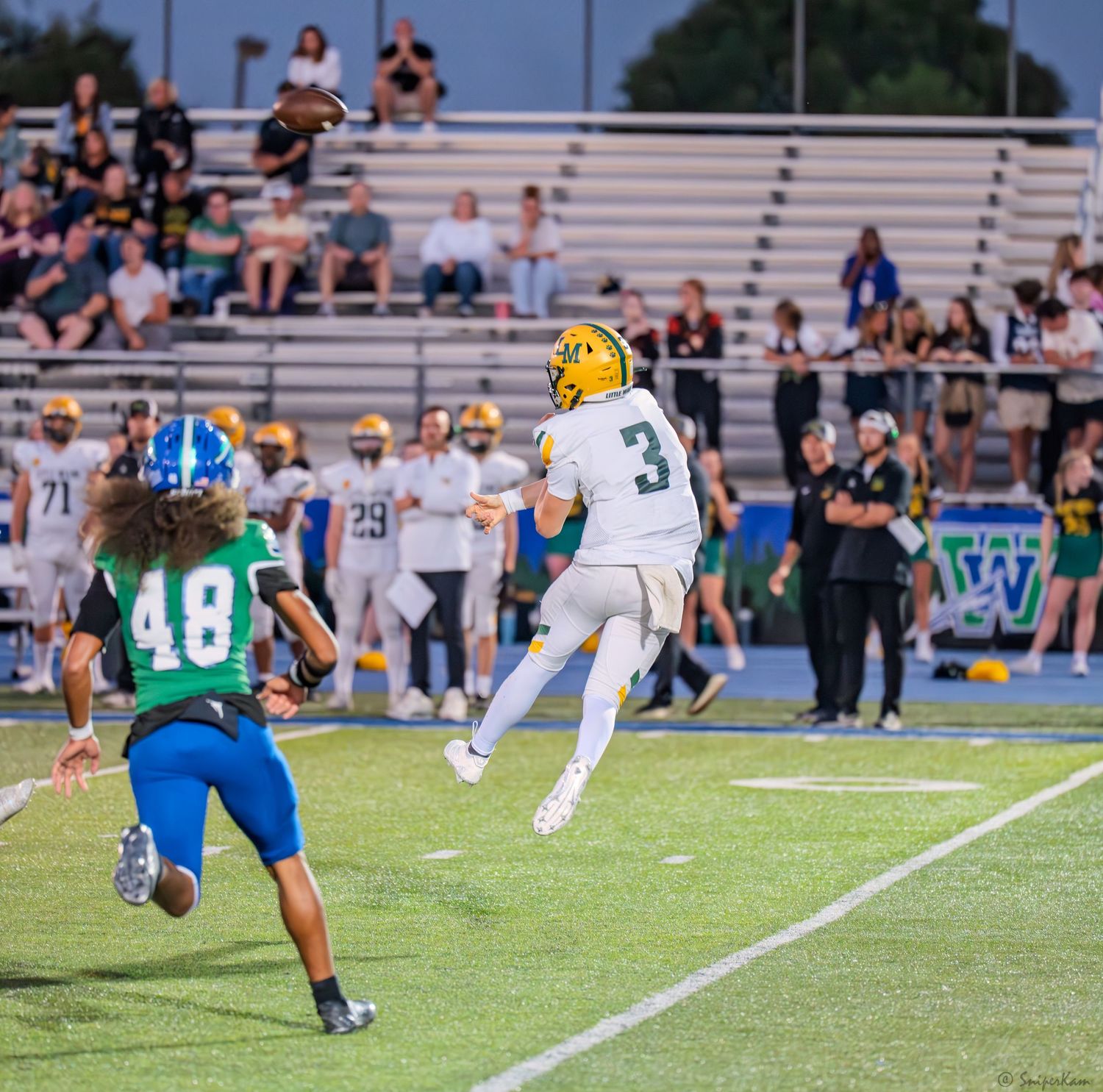 High school football player number 3 leaps to catch pass while defender number 48 in blue uniform defends.