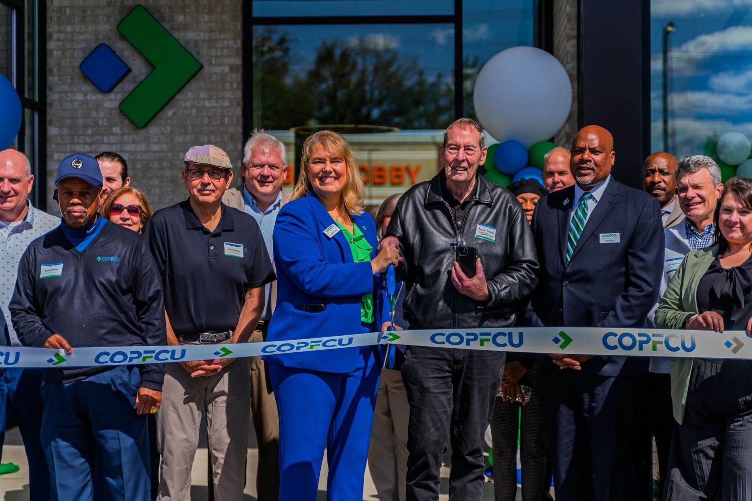 COPFCU ribbon cutting ceremony with smiling group outside new credit union branch.