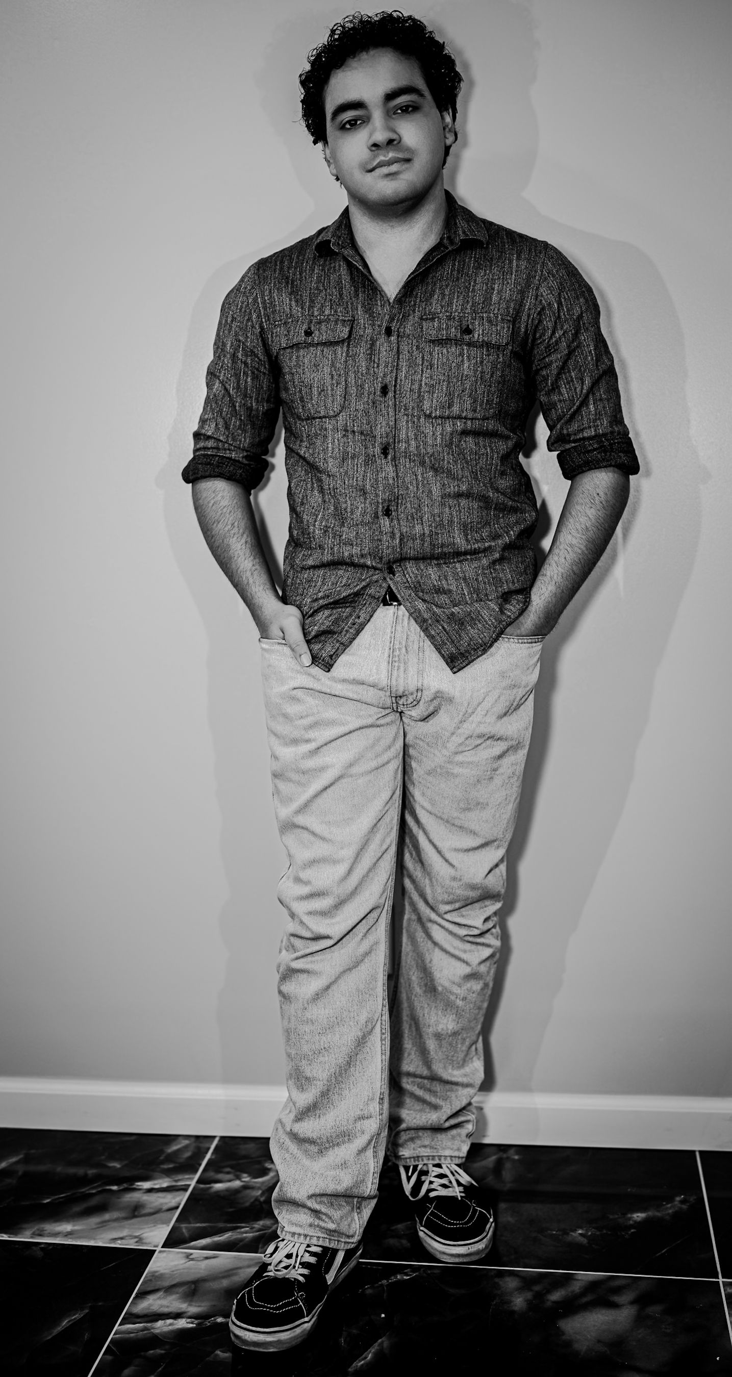 Black and white full body portrait of young man in button-up shirt and jeans.