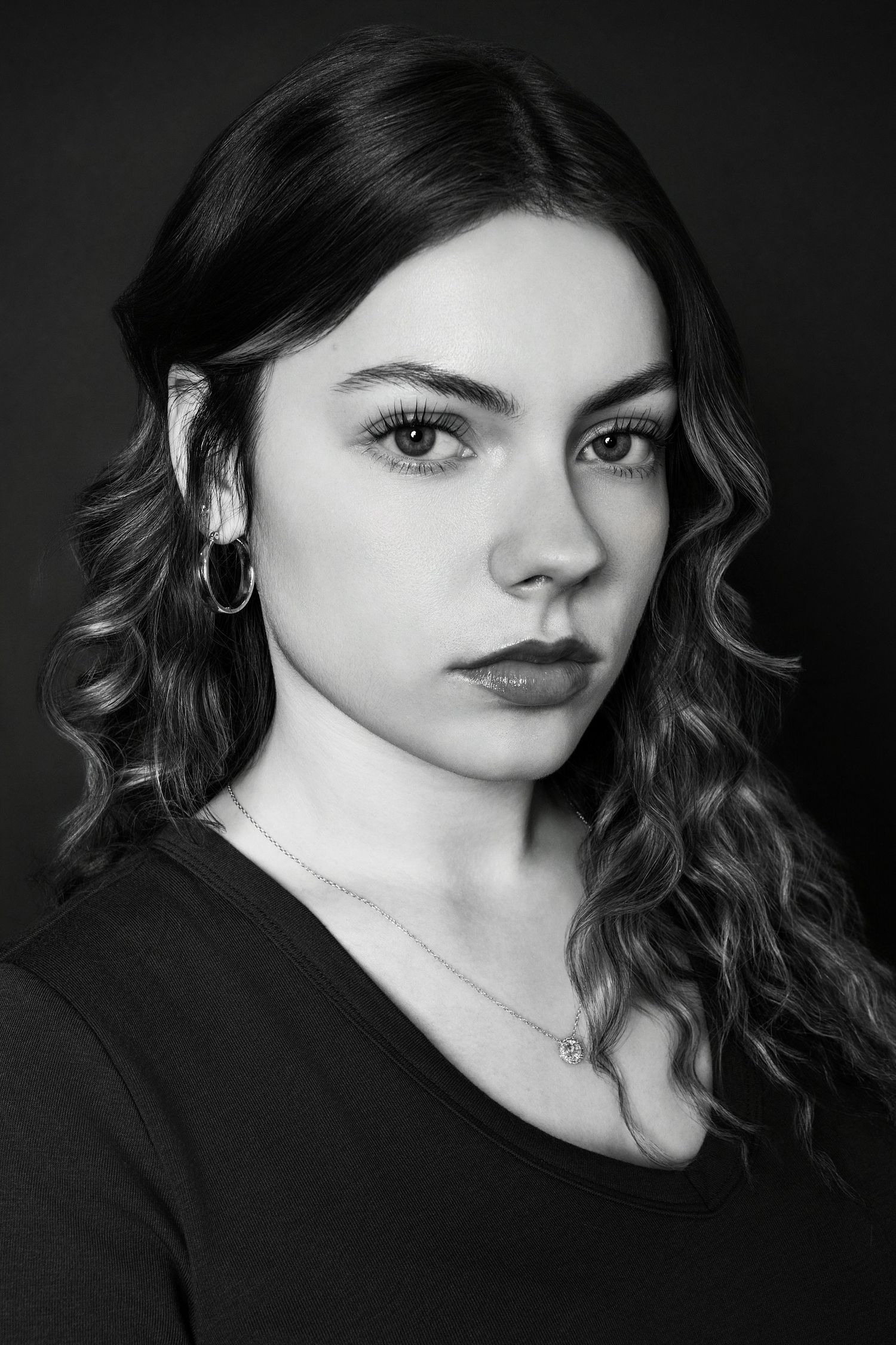 Black and white portrait of a young woman with curly hair and hoop earring wearing a black top.