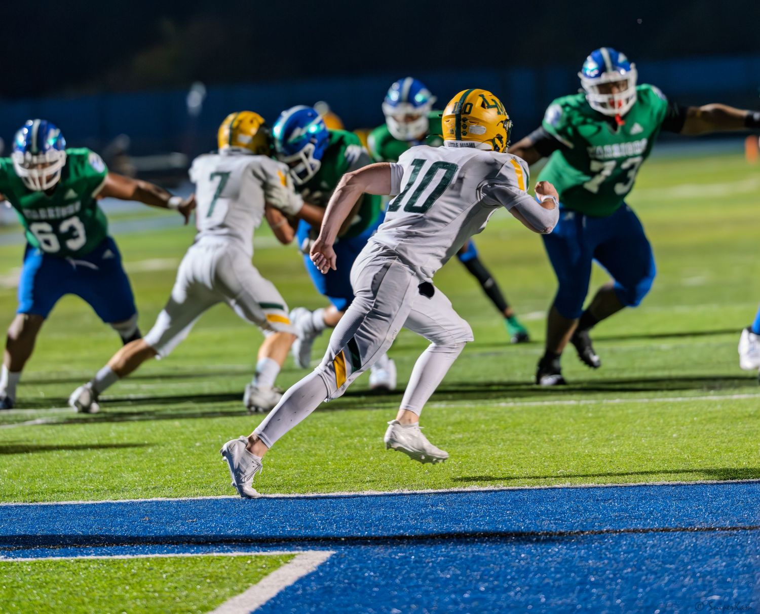 A football player in gold uniform runs toward the end zone during a night game.