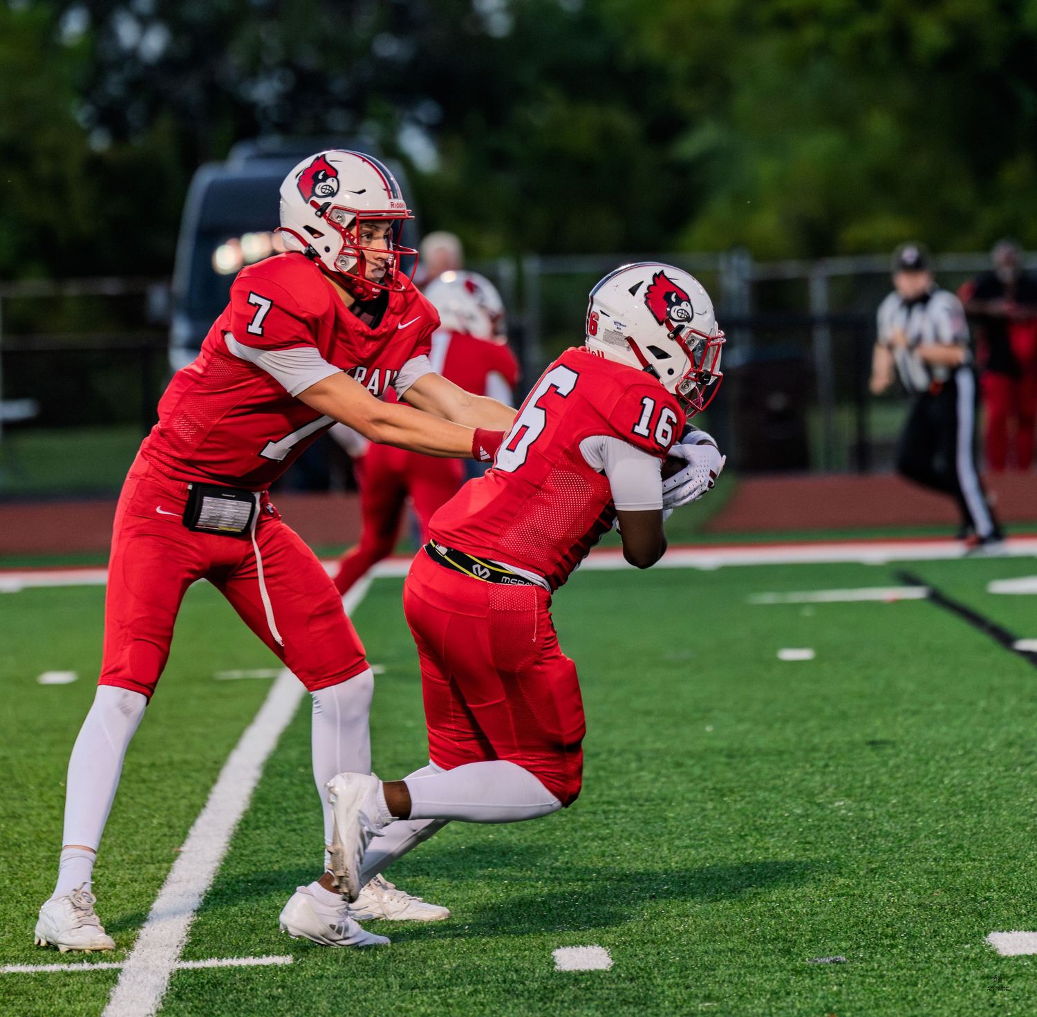 Red team quarterback #7 executes a handoff to teammate #16 during a high school football game.
