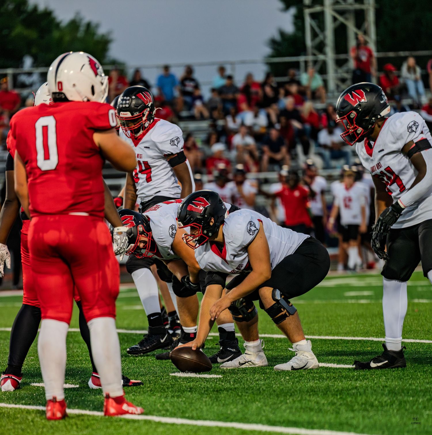A football team lines up at the line of scrimmage preparing for a play during a high school game.