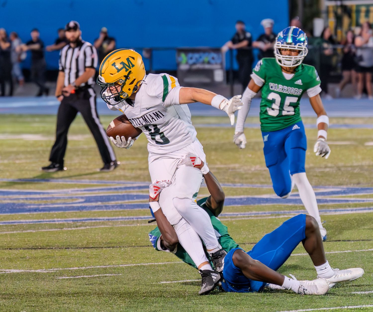 A yellow-uniformed football player breaks a tackle during a high school night game.