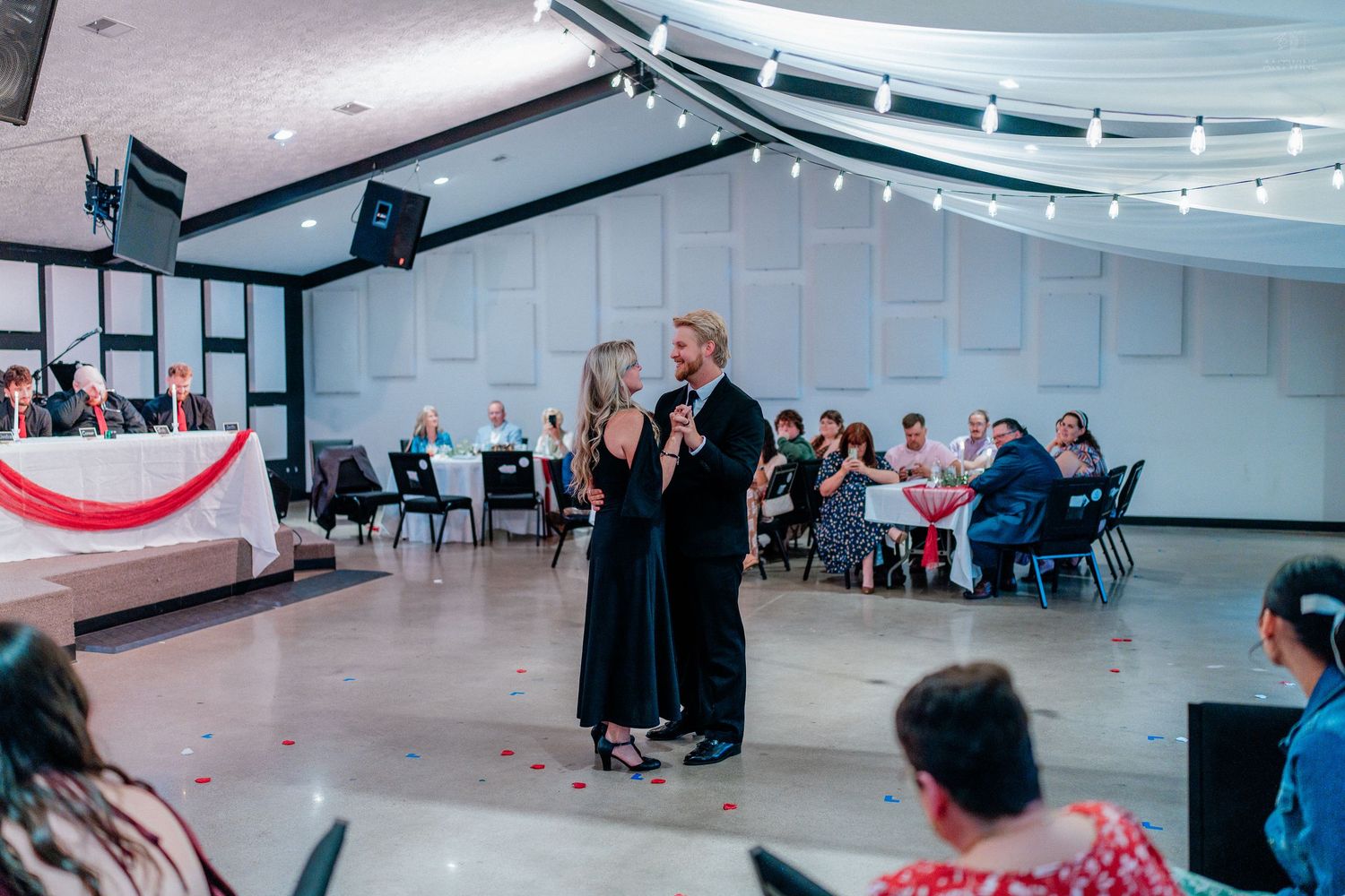 Couple shares parent dance on open floor at wedding reception with seated guests watching.