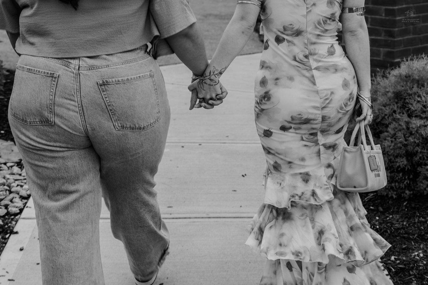 Close-up black and white photo of two women holding hands while walking together.