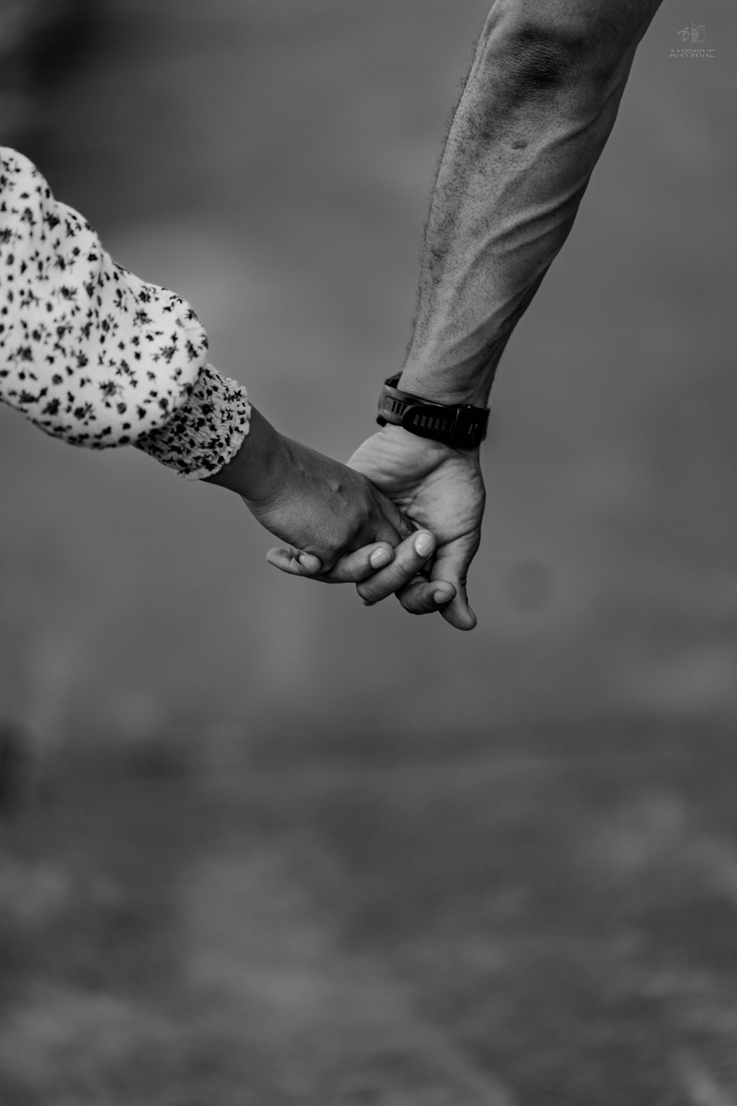 Close-up black and white photo of a couple holding hands, man wearing a black watch.